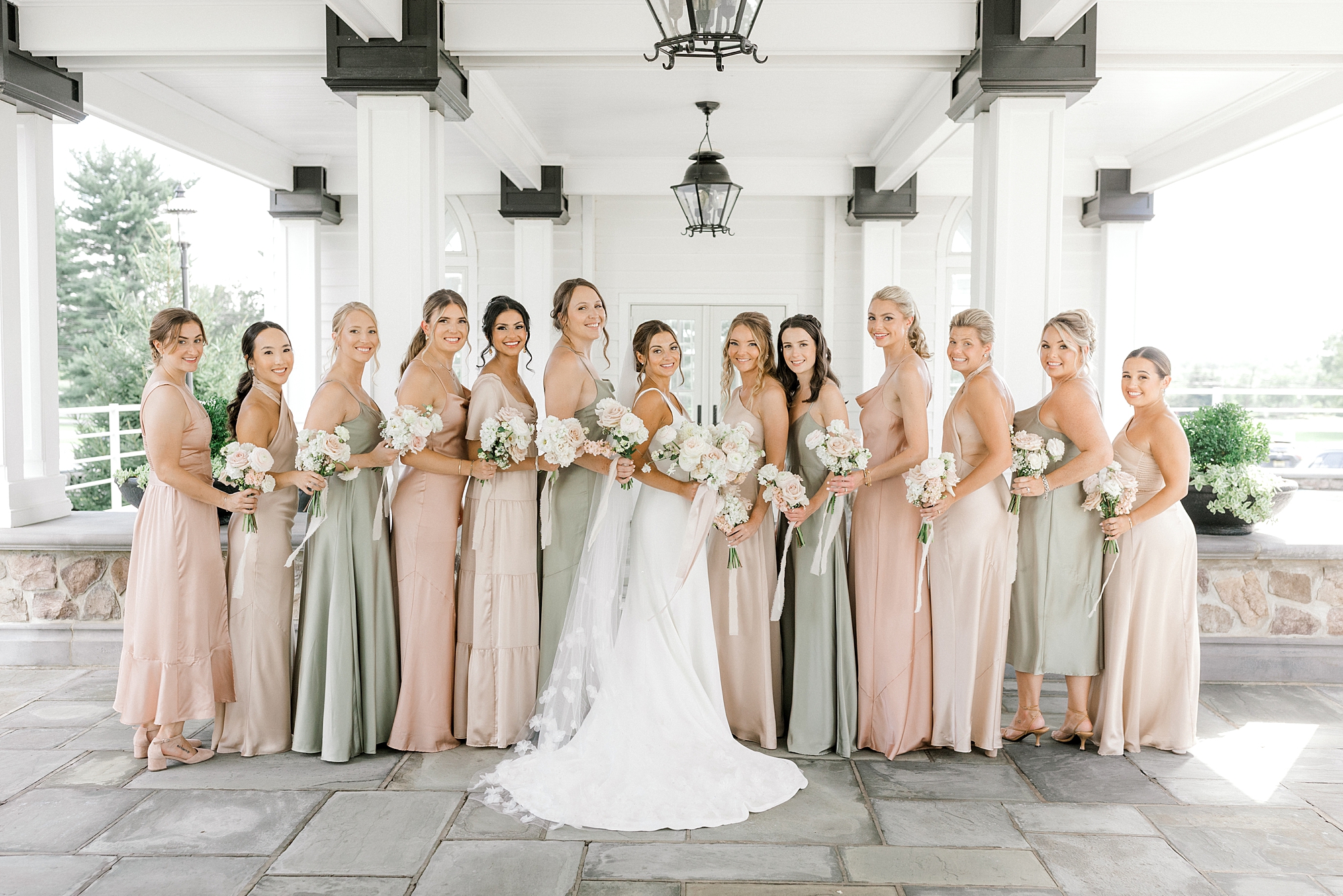 bride poses with 12 bridesmaids in soft pink and green dresses