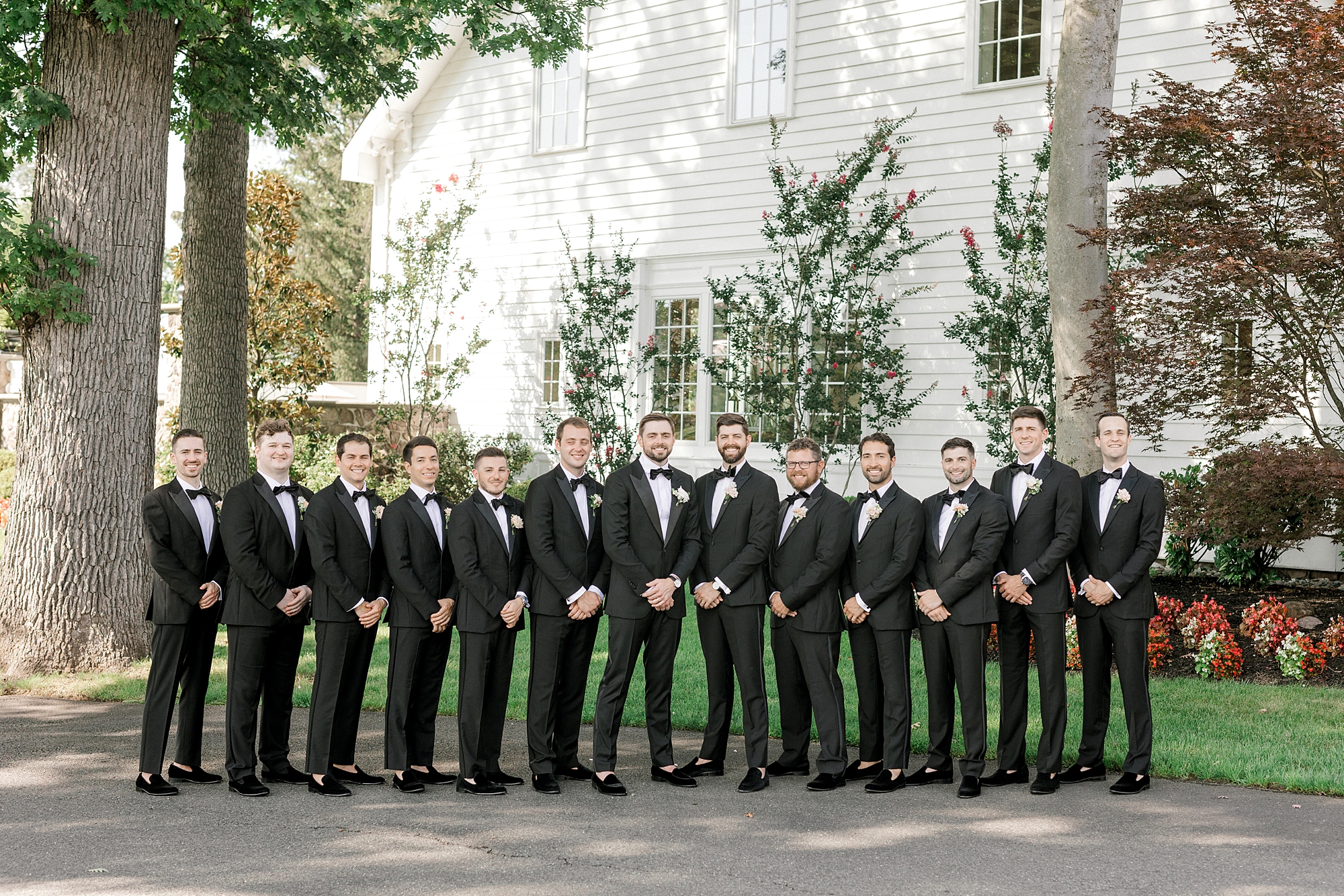 groom stands with groomsmen in black suits in front of Ryland Inn