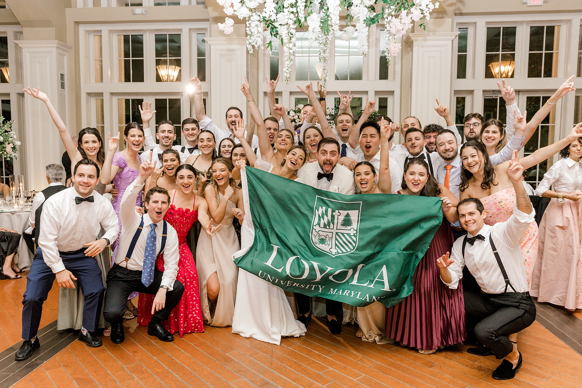 bride and groom pose holding Loyola flag with guests at reception