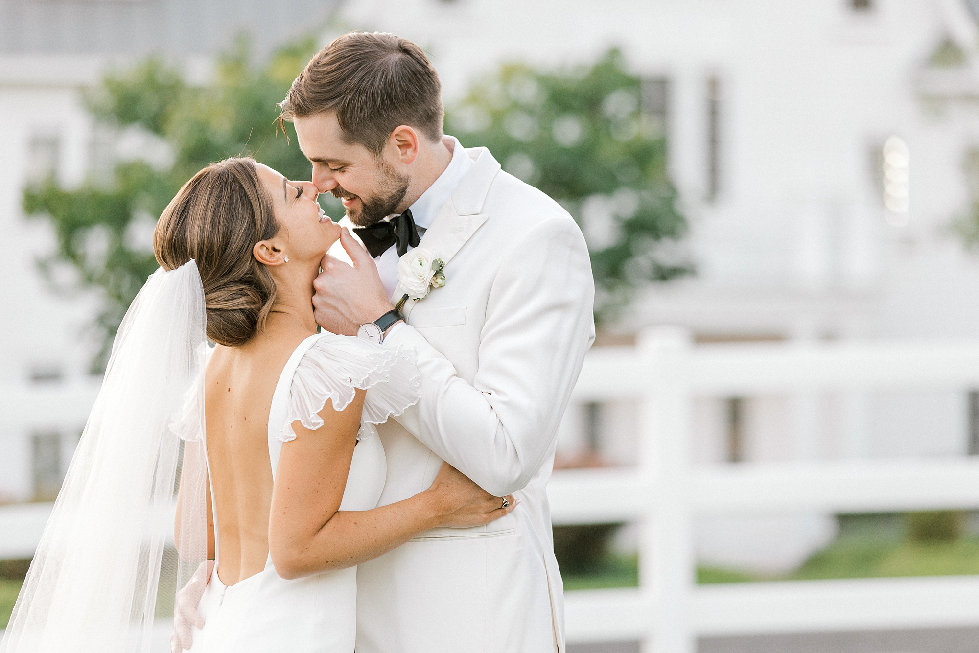 groom in white suit jacket leans to kiss bride in field at Ryland Inn