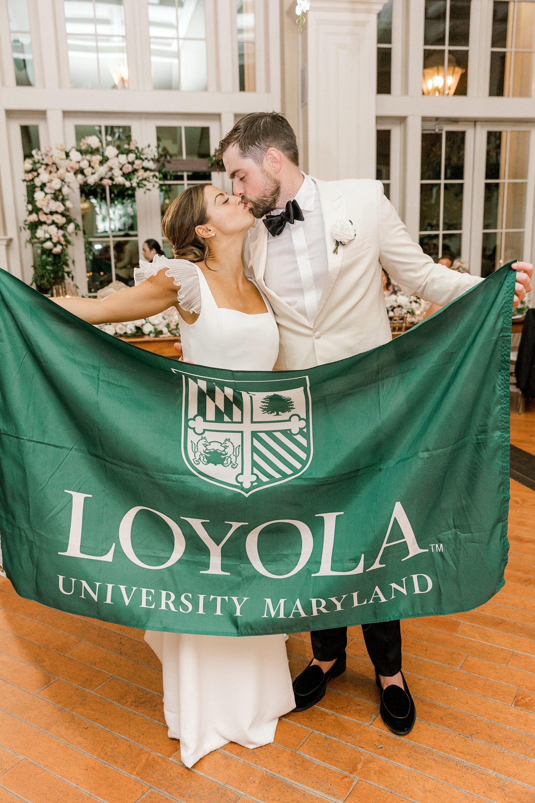bride and groom kiss holding green Loyola flag during NJ wedding reception