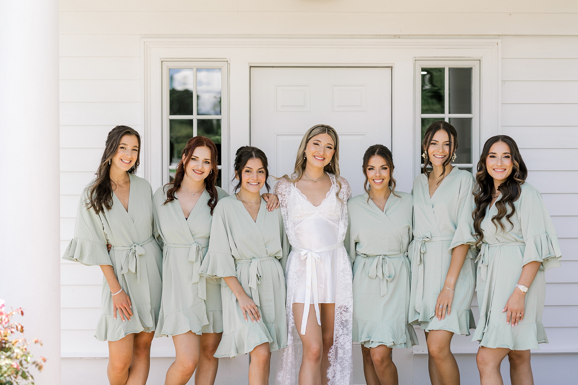 bride poses with bridesmaids in pale green robes outside Ryland Inn