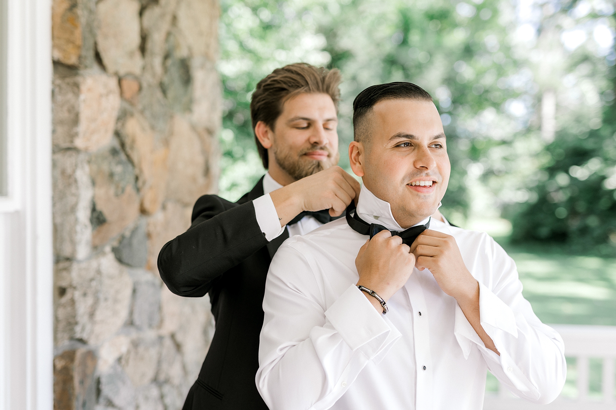 groomsman helps groom adjust black bow tie before NJ wedding