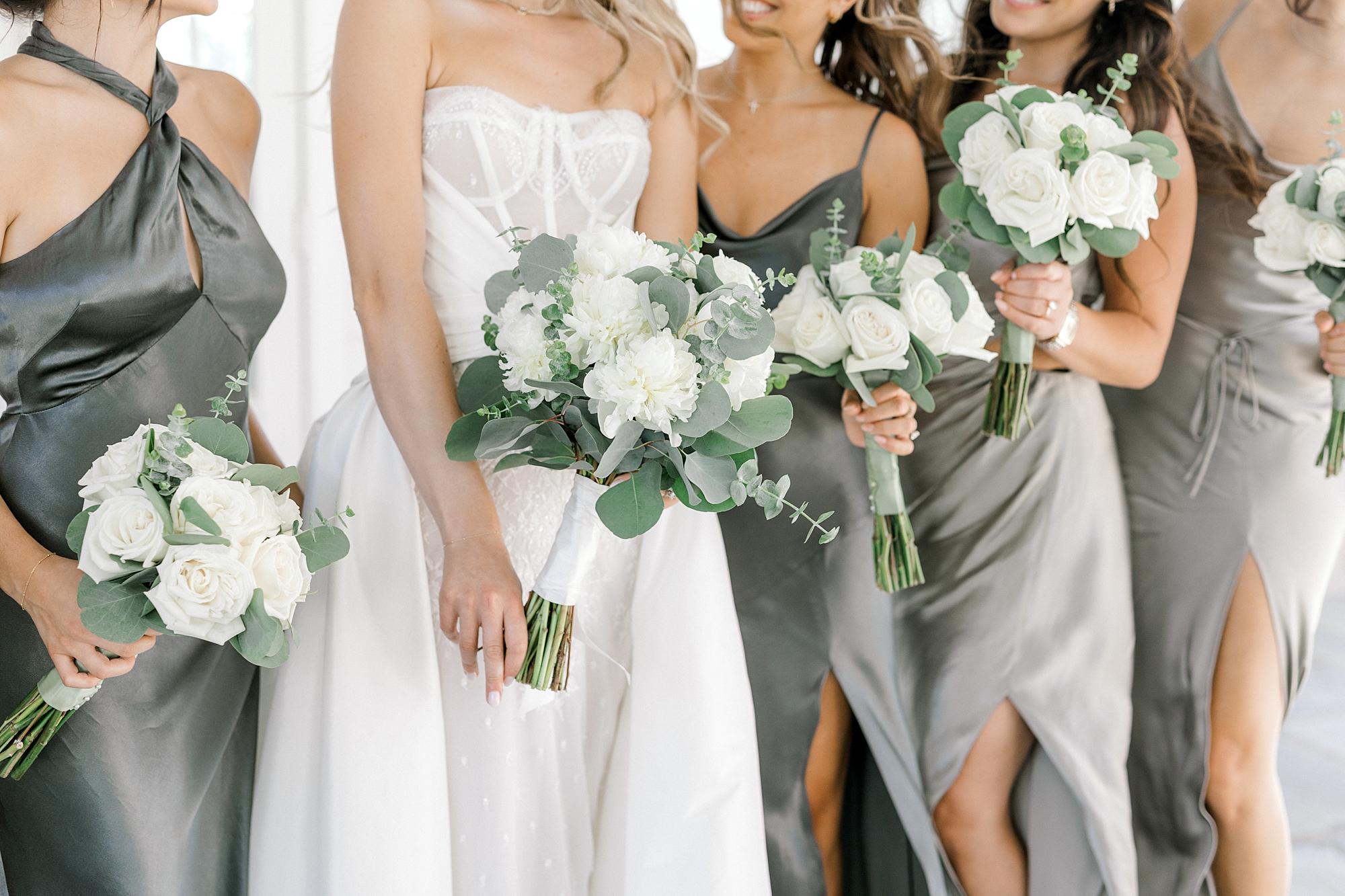 bride poses with bridesmaids in sage green gowns with white bouquets