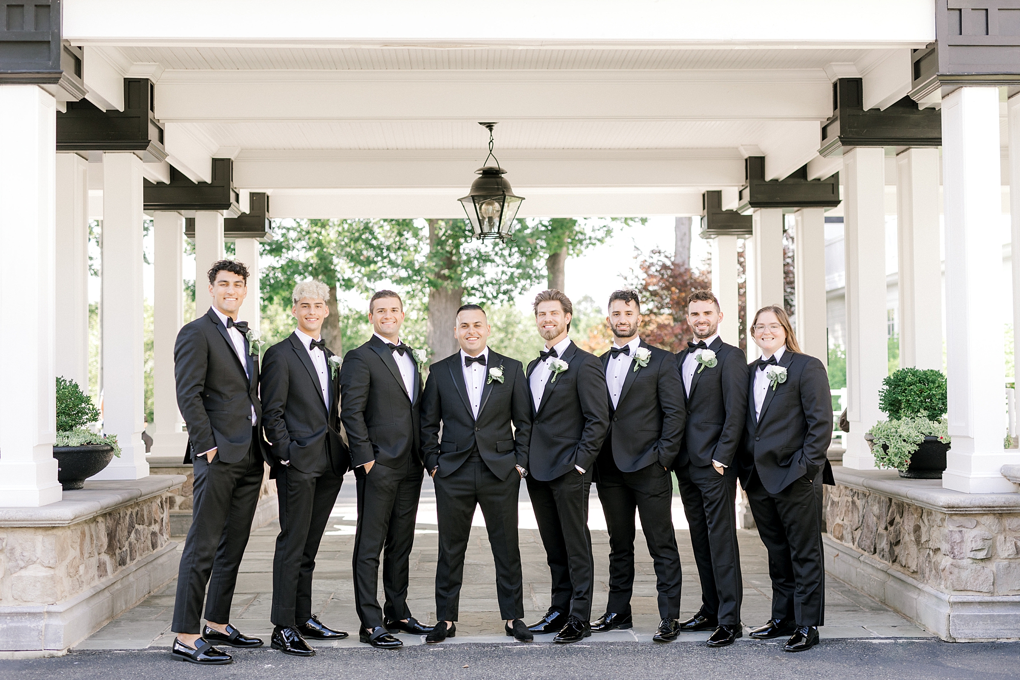 groom stands with groomsmen in black suits outside Ryland Inn