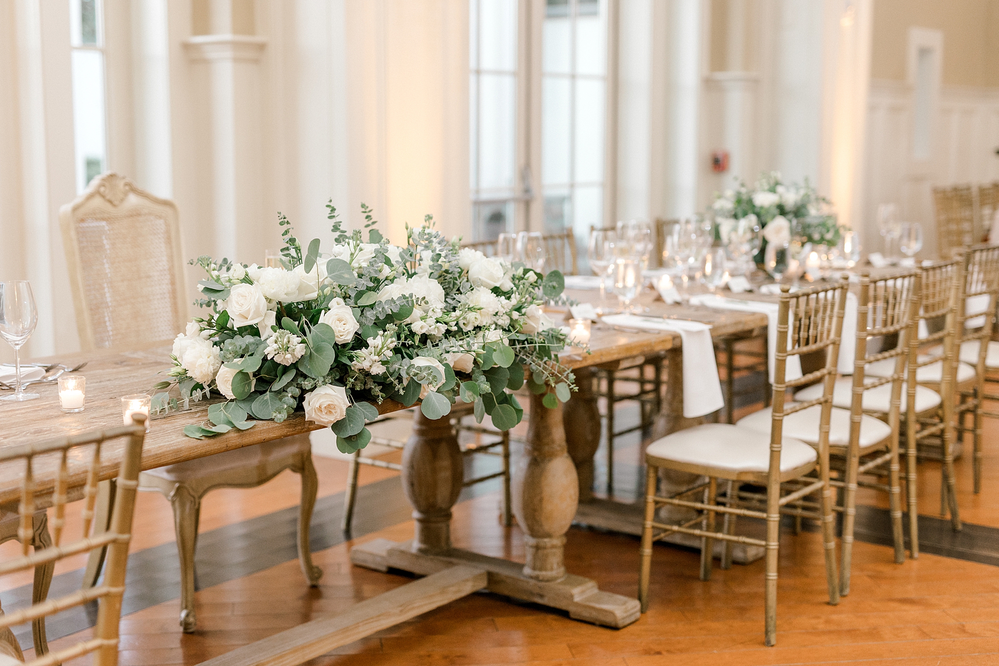 wooden tables with white rose centerpieces and white napkins