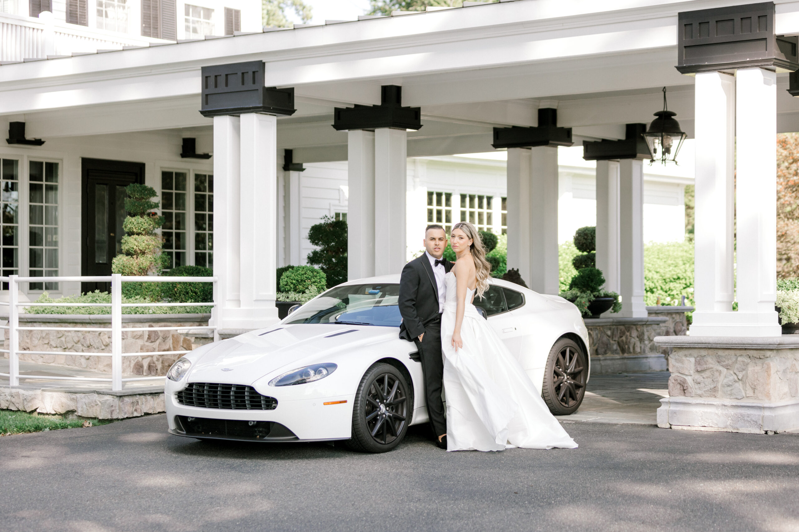 newlyweds lean against white Aston Martin outside Ryland Inn