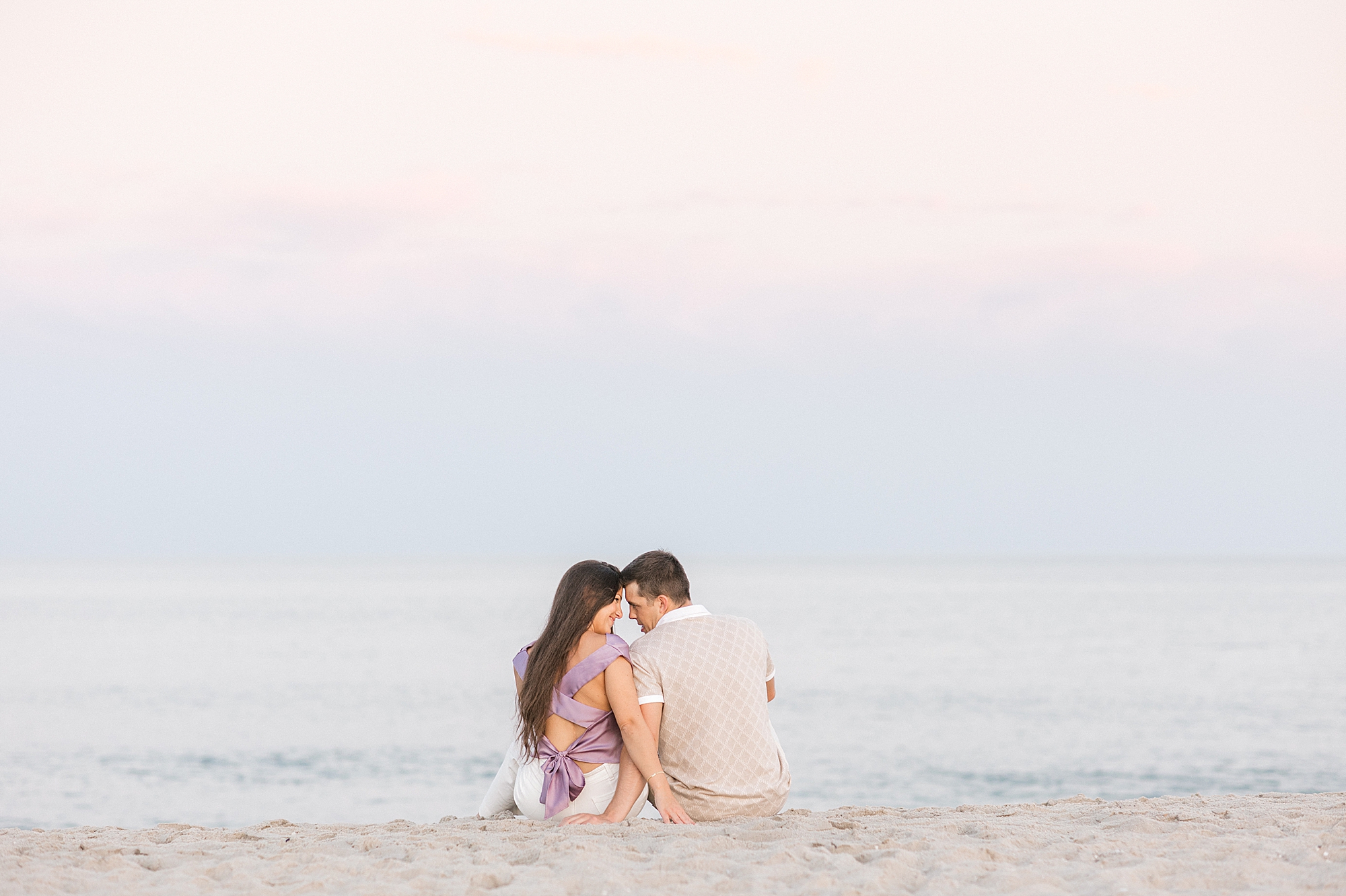 man and woman sit on beach during Historic Cape May beach engagement session