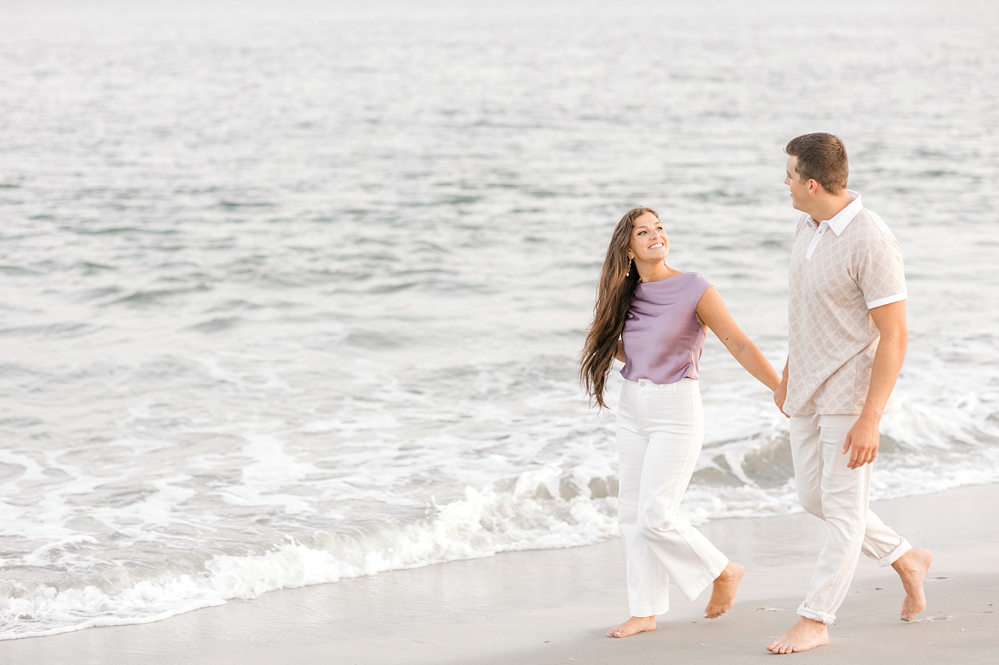 engaged couple hold hands walking along ocean