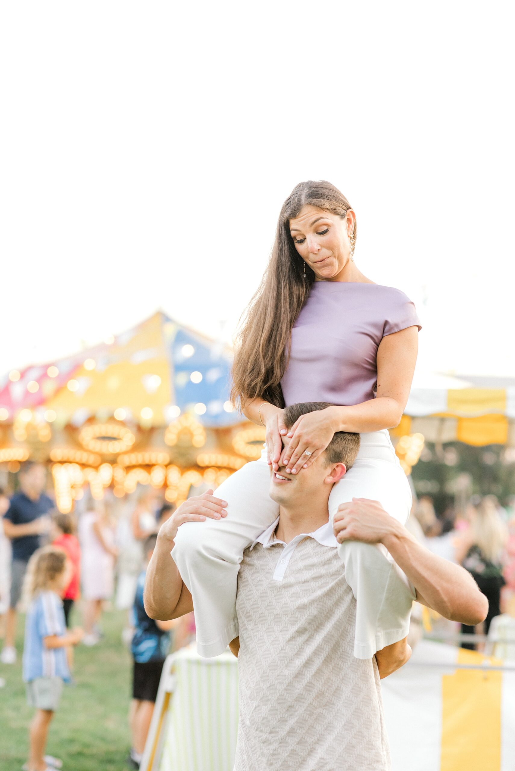 woman in purple top sits on man's shoulders during Historic Cape May engagement session at carnival