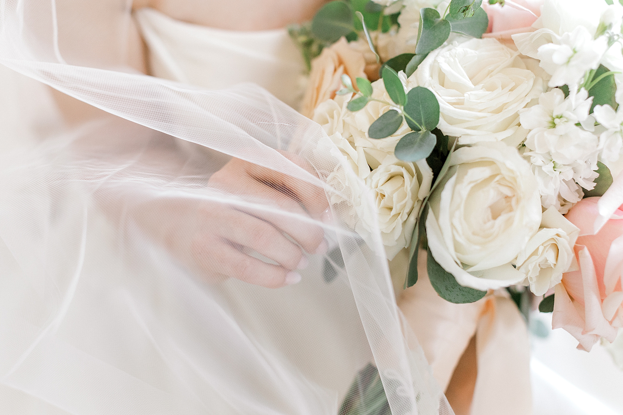 bride holds bouquet of ivory roses and veil around bouquet