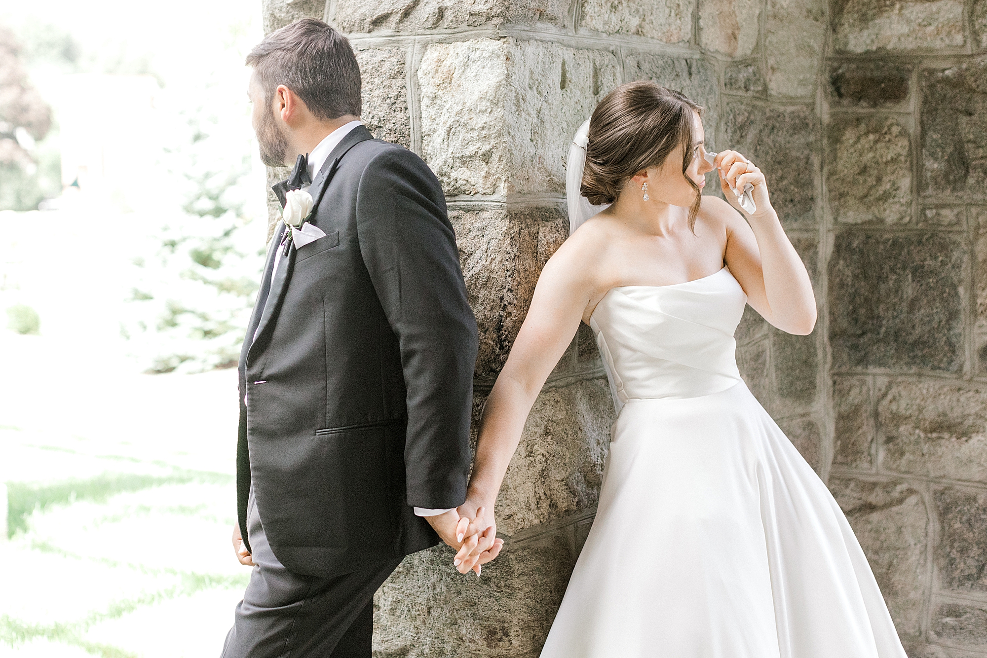bride and groom hold hands around corner of stone pillar at church for first touch