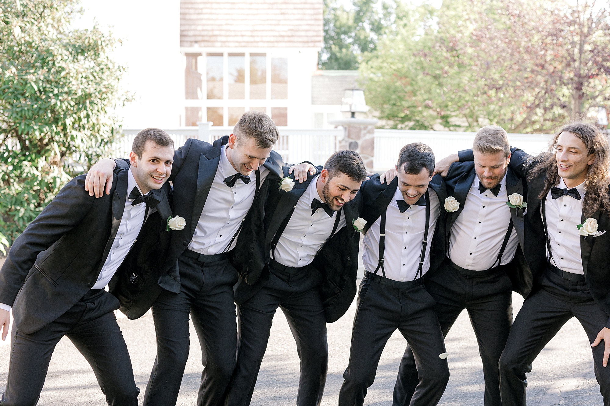 groom hugs groomsmen in black tuxes leaning and laughing