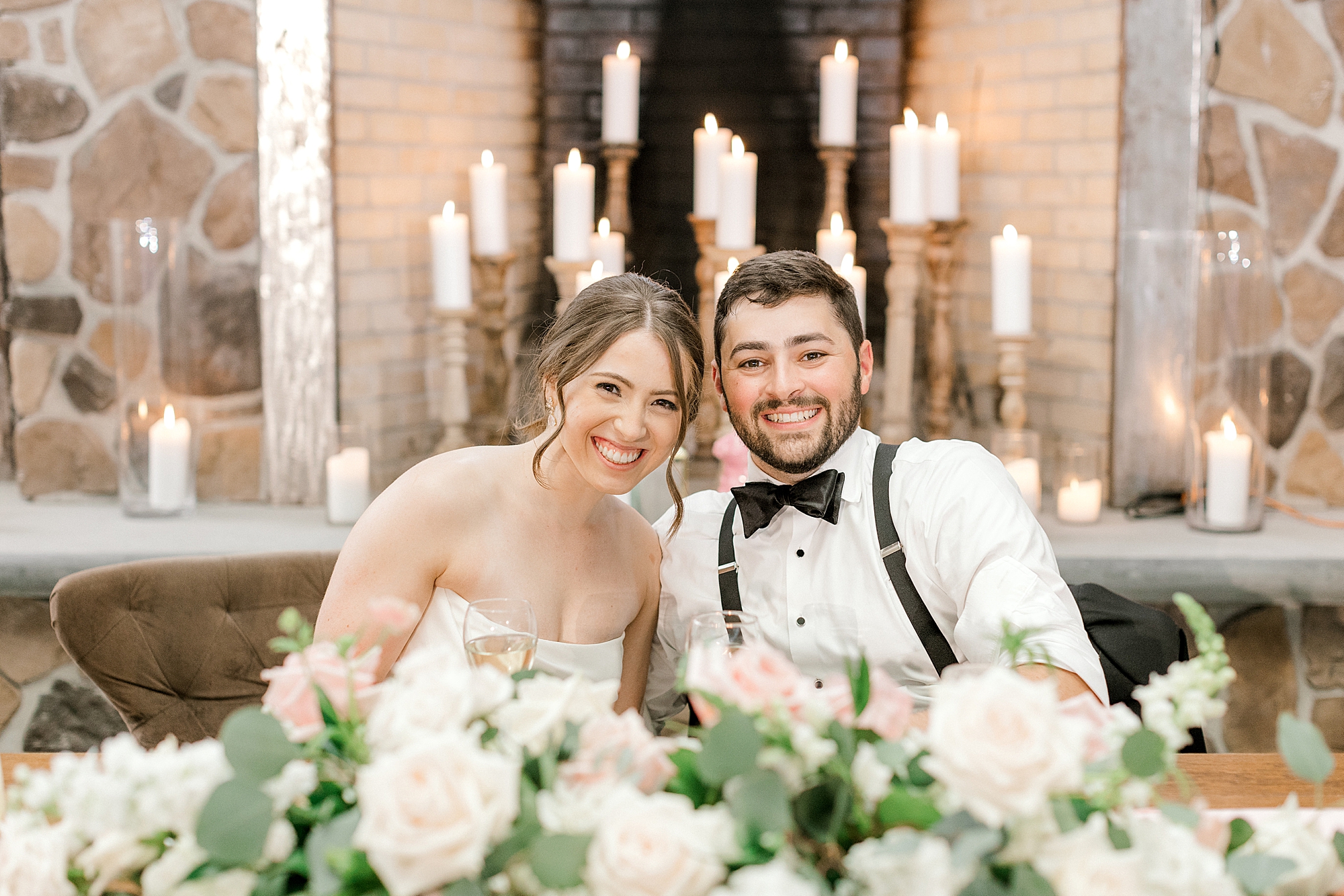 newlyweds sit together at sweetheart table in front of gold candlesticks