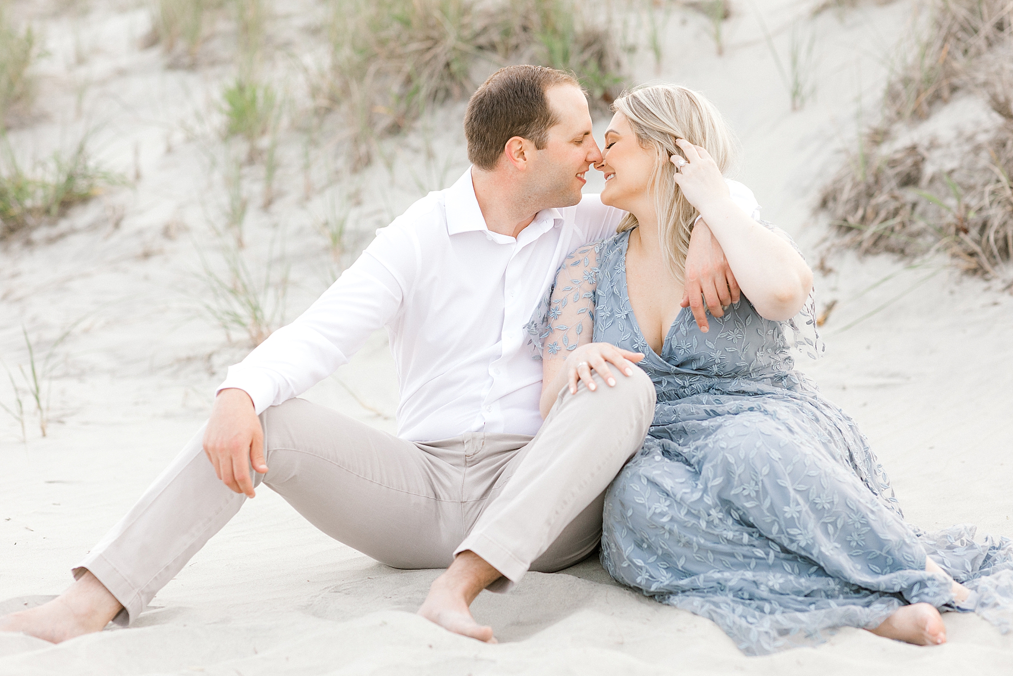 engaged couple sits on dunes leaning for a kiss at Ventnor Beach