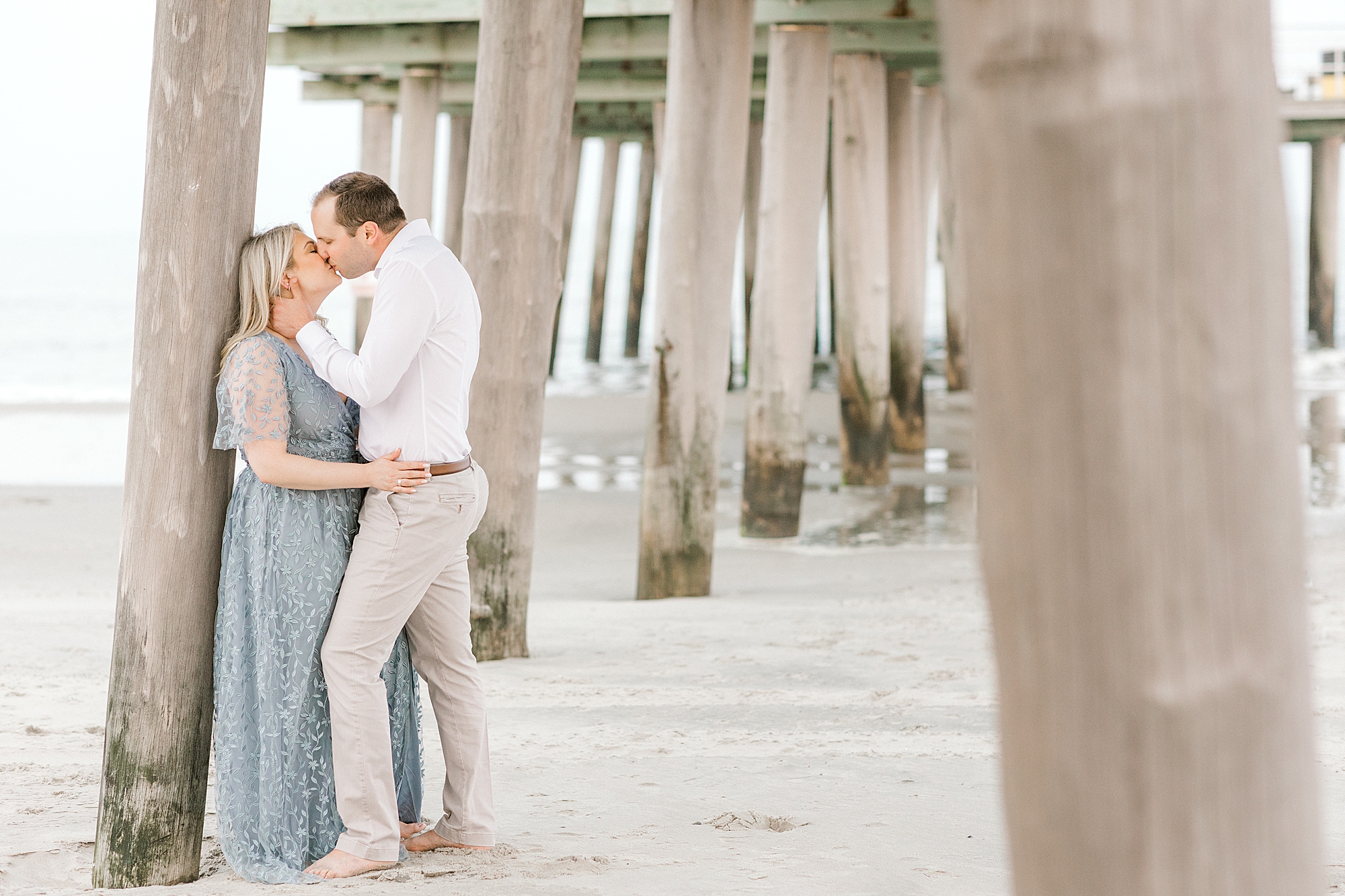 man leans kissing woman against dock pillars at Ventnor Beach