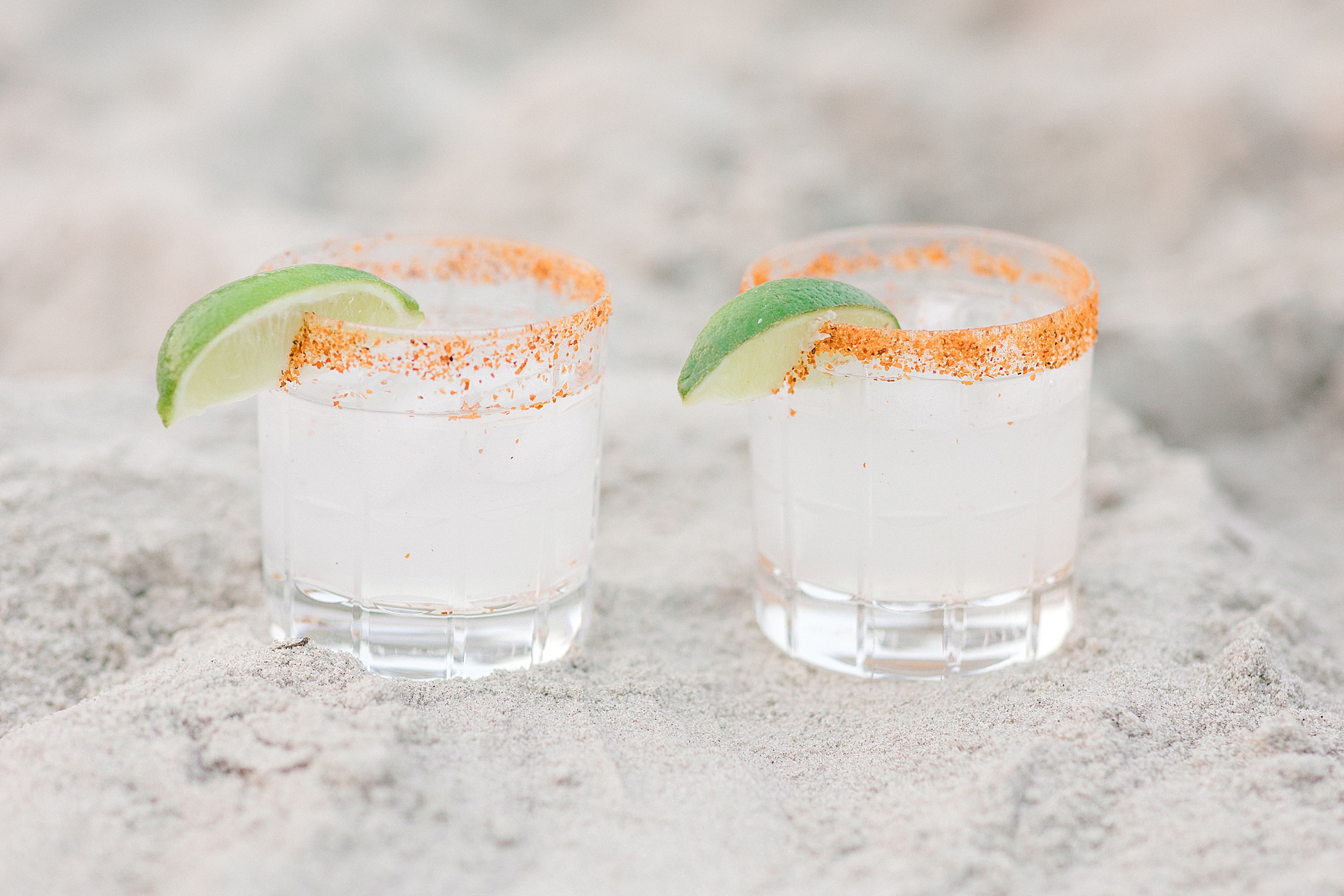 two margaritas with orange rims and lime wedges