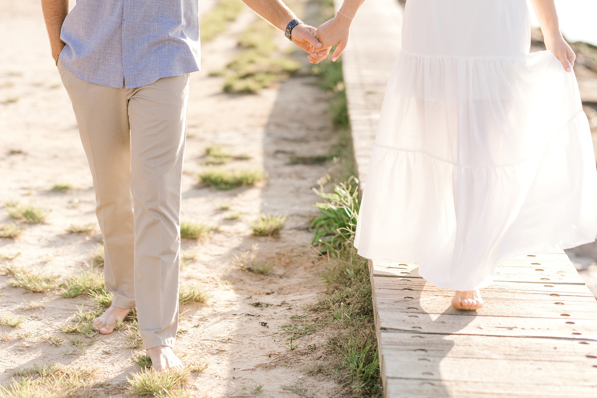 couple holds hands walking along pathway near Barnegat Lighthouse on Long Beach Island