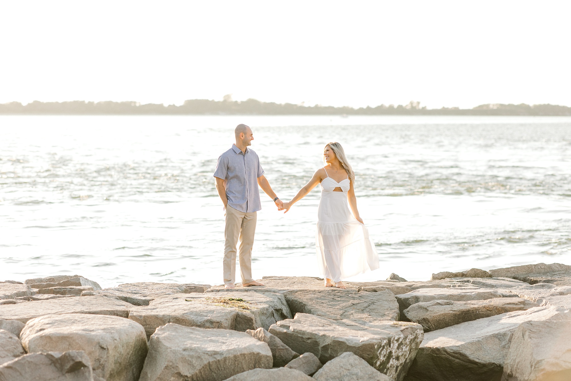engaged couple holds hands smiling at each other standing on rocks