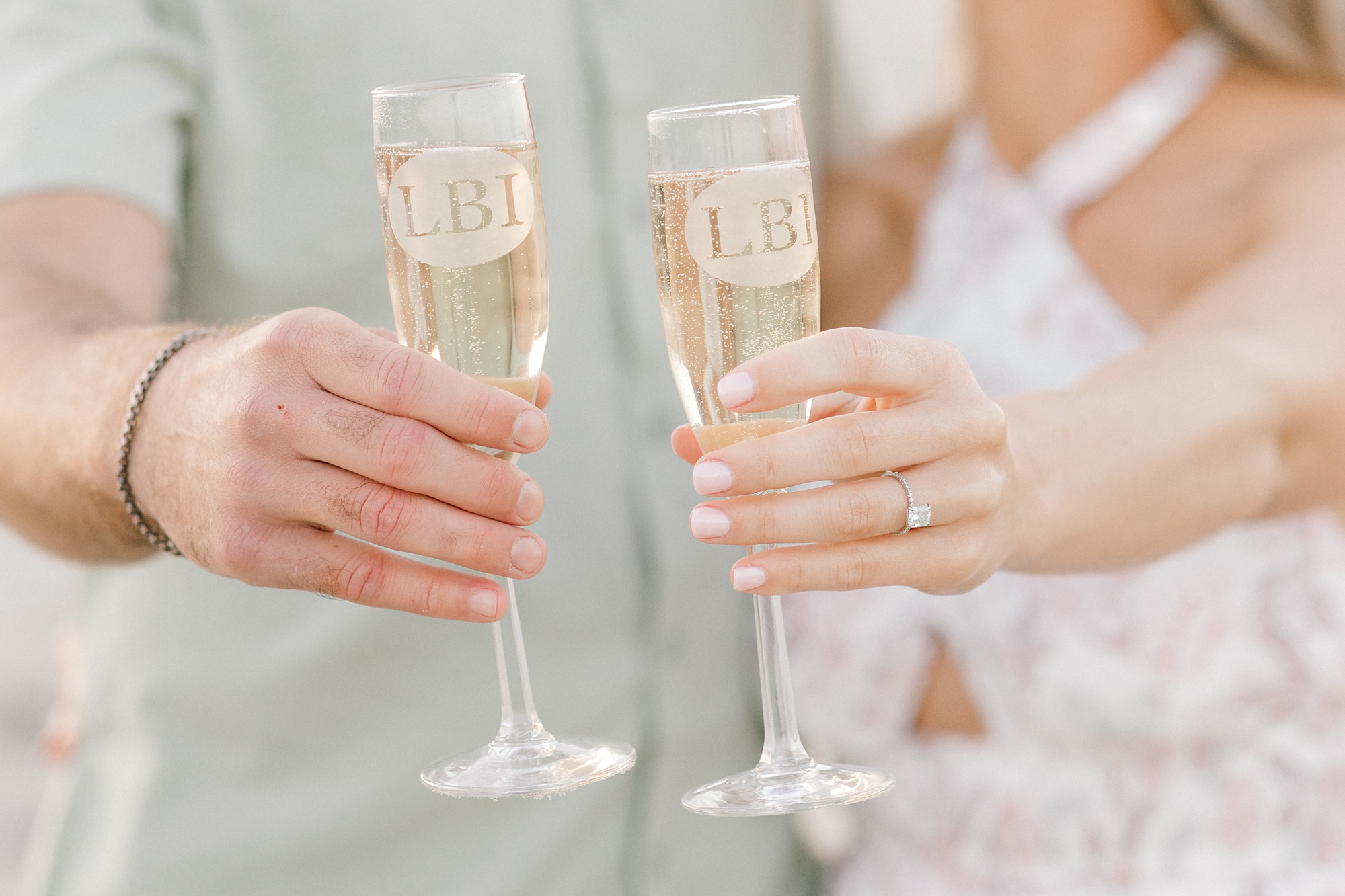 engaged couple holds LBI champagne glasses showing off bride's ring