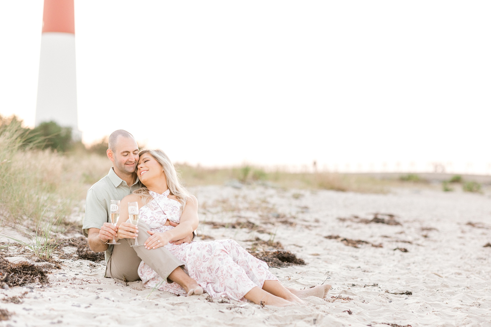 engaged couple snuggles on beach in front of Barnegat Lighthouse