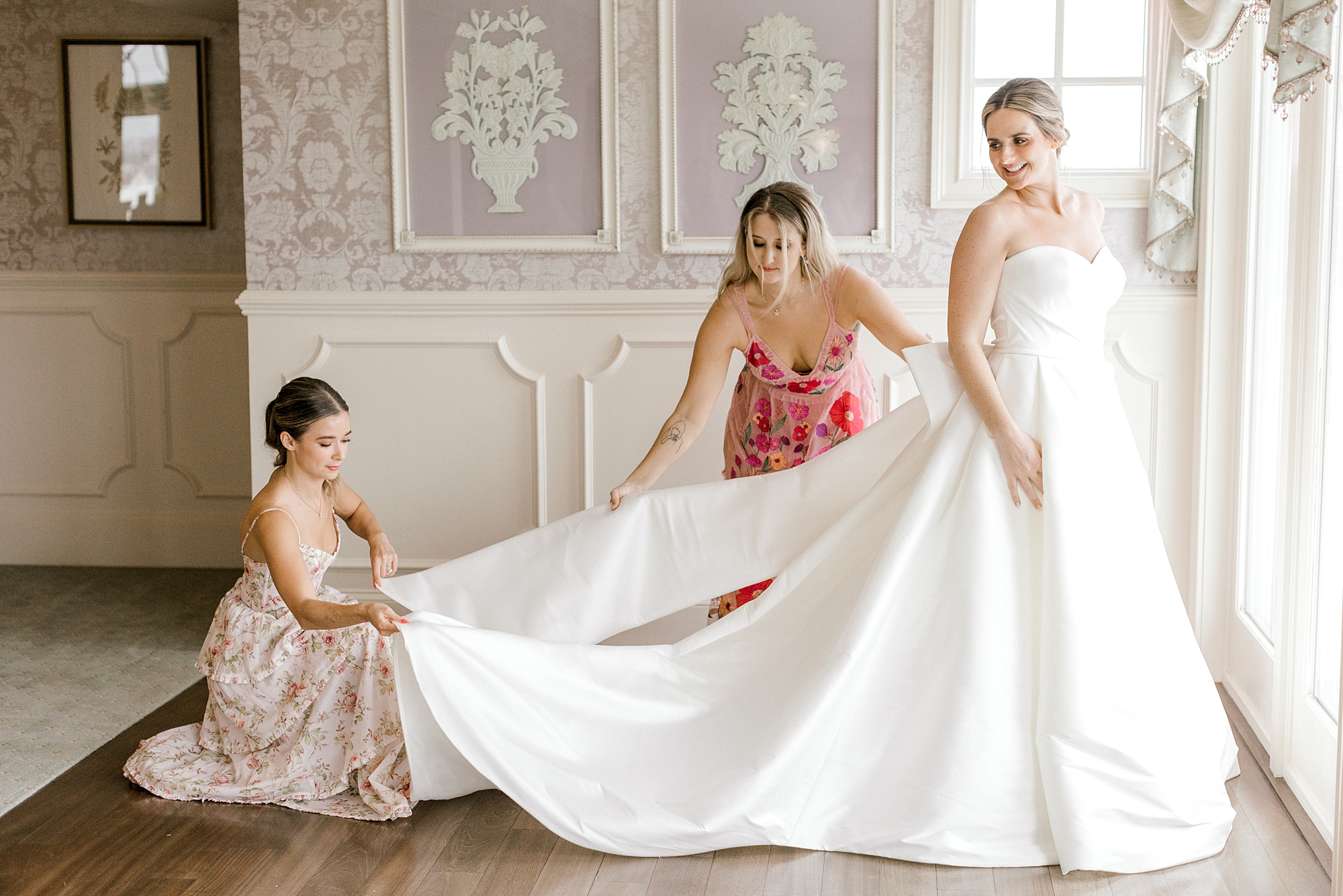 bridesmaids help bride into wedding gown with big bow at Mallard Island Yacht Club
