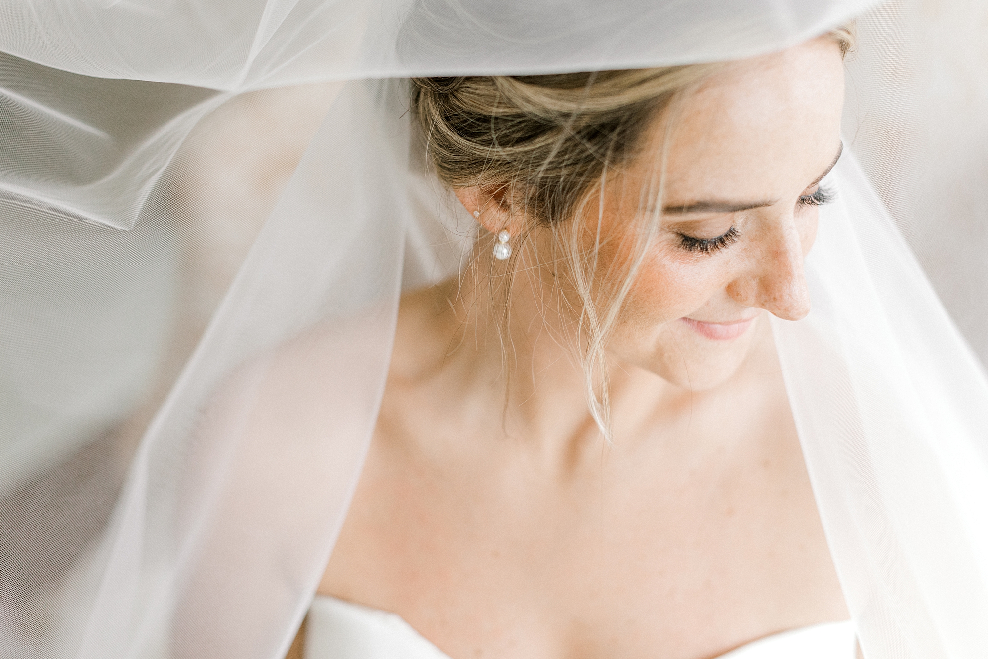 bride looks down over wedding gown with veil around shoulders
