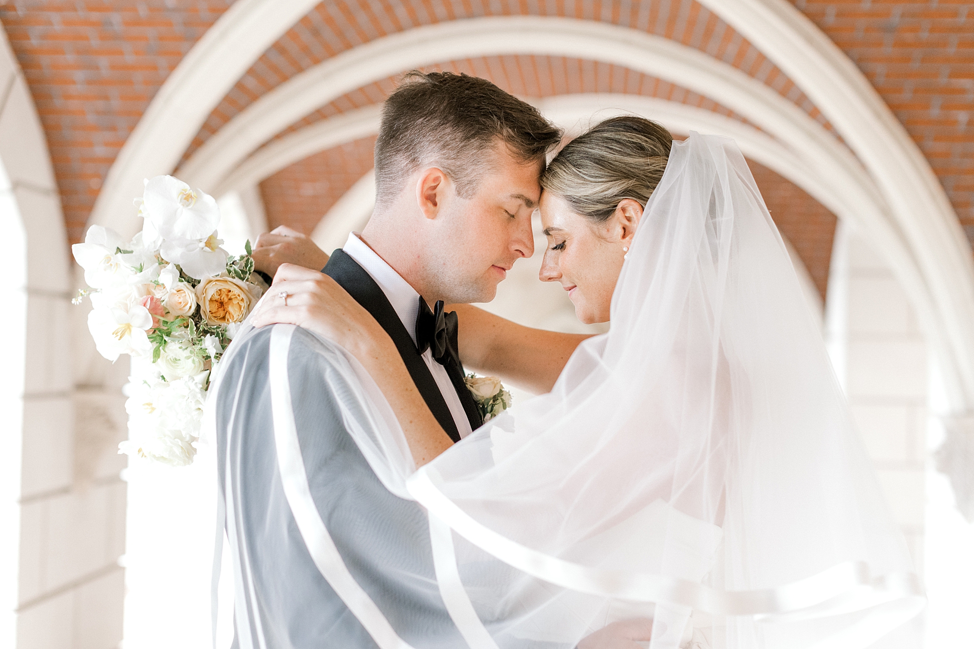 newlyweds hug leaning heads together with veil around their shoulders