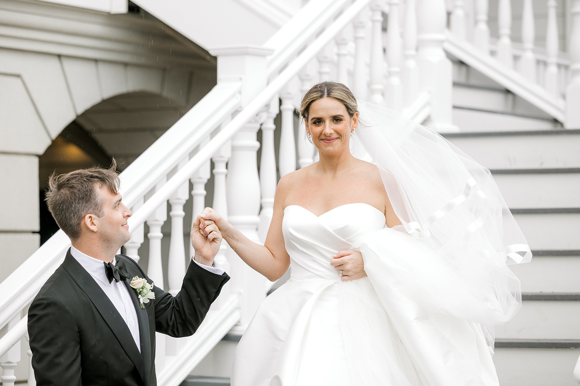 groom helps bride down steps outside Mallard Island Yacht Club