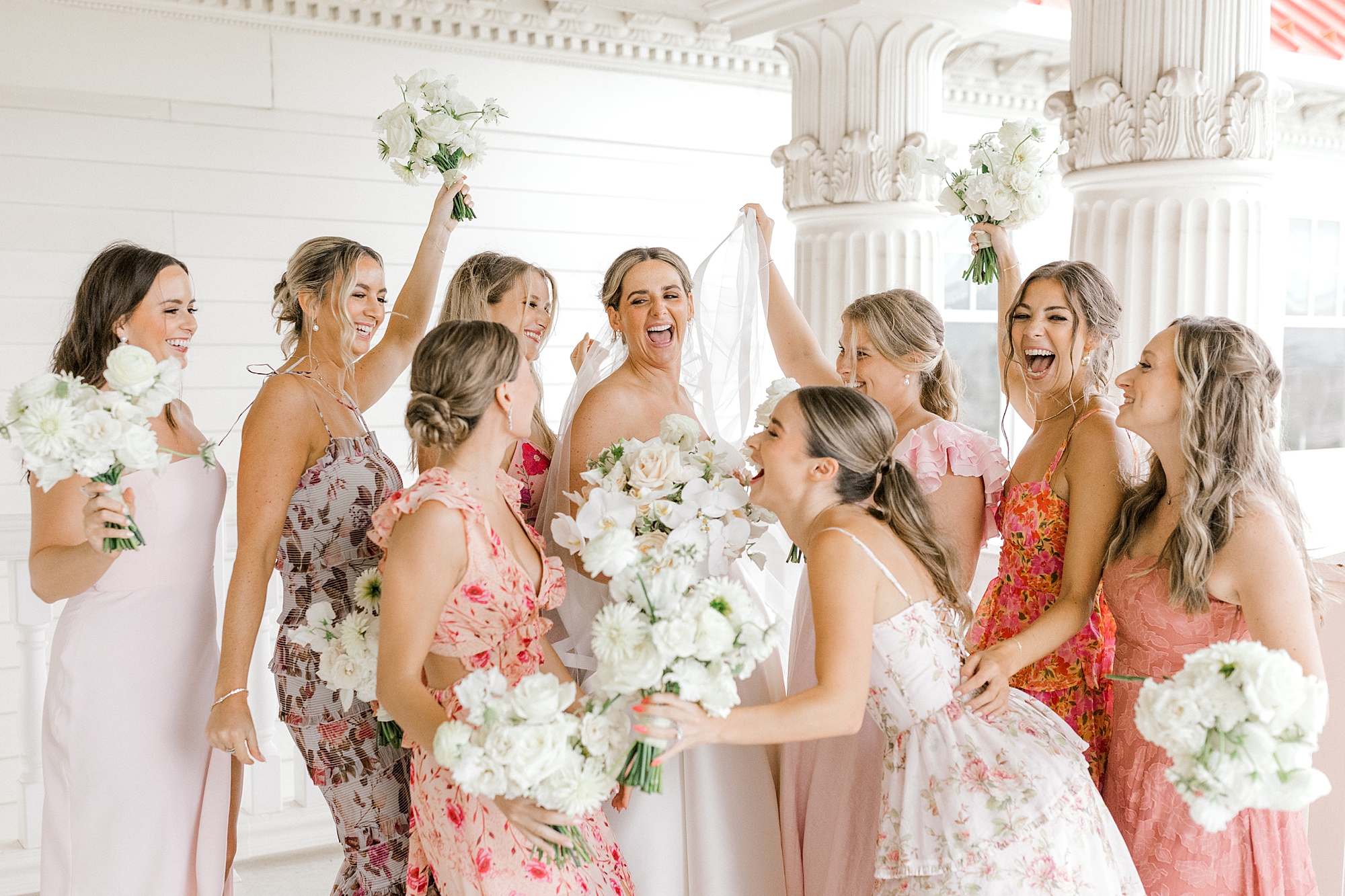 bride laughs with bridesmaids in mismatched pink and peach gowns at Mallard Island Yacht Club