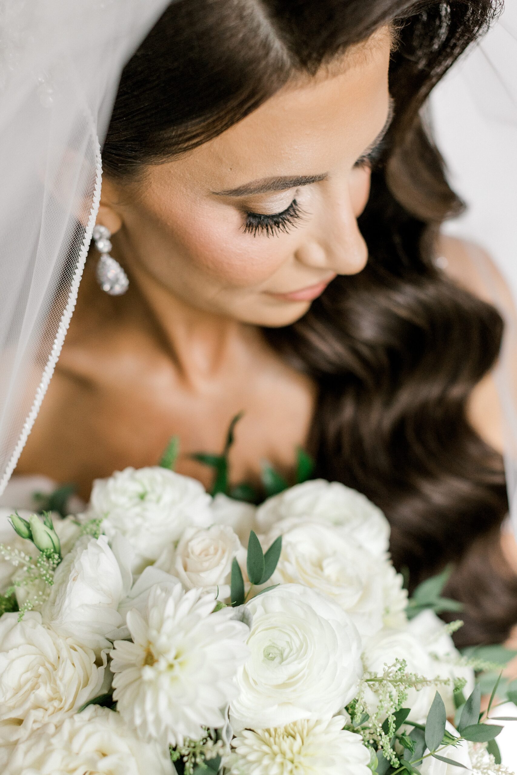 bride looks down at bouquet of white roses during fall wedding