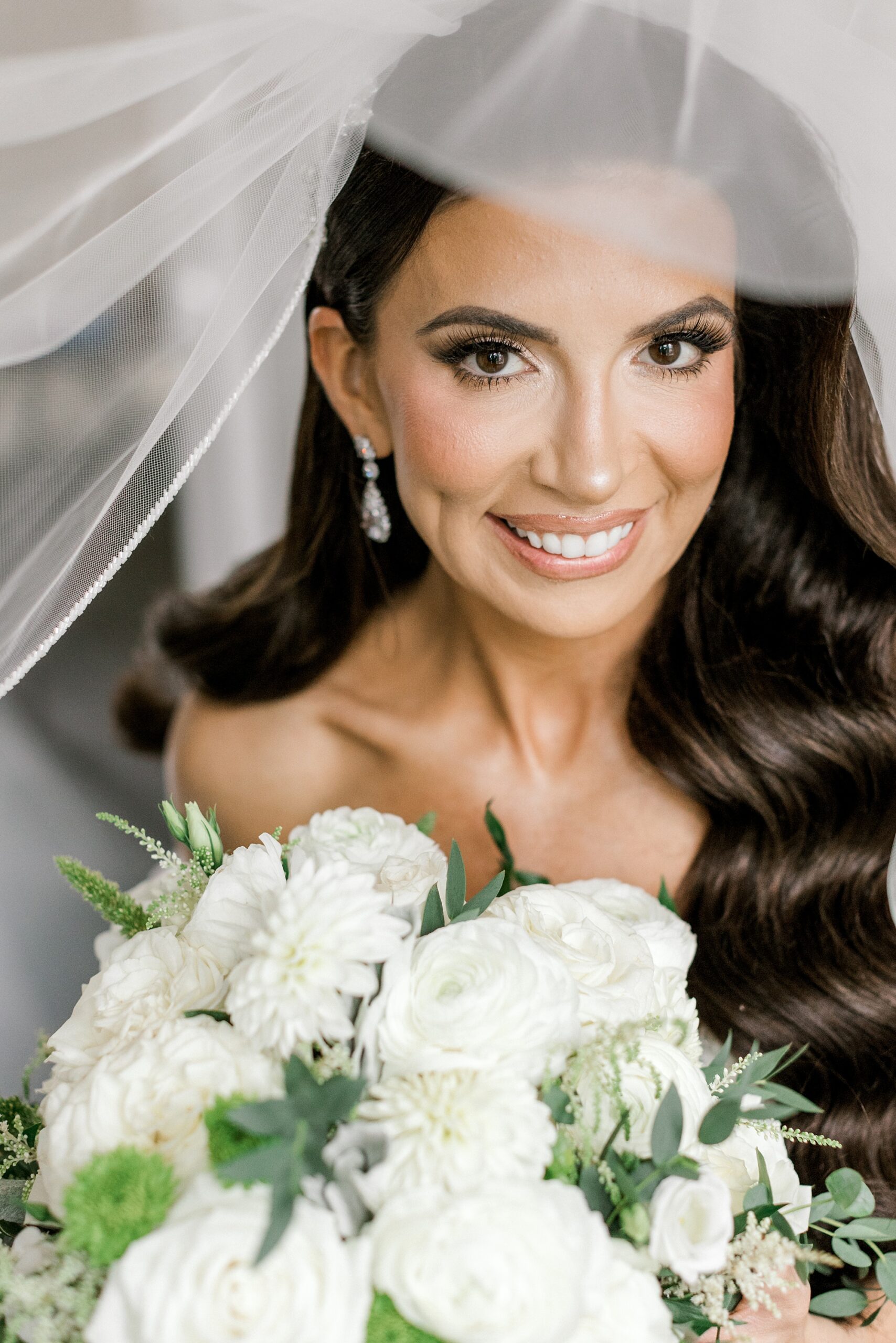 bride smiles under veil holding bouquet of white flowers for fall wedding