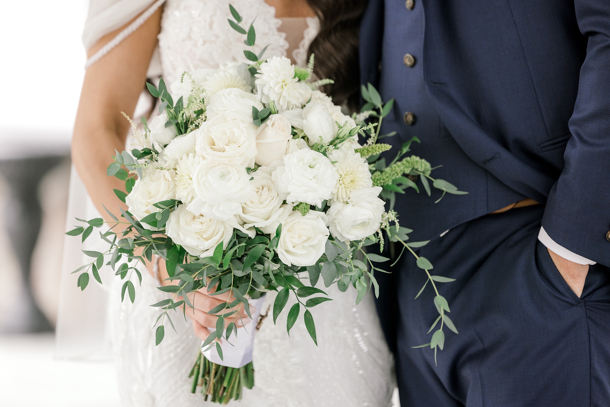 bride holds bouquet of white roses and greenery