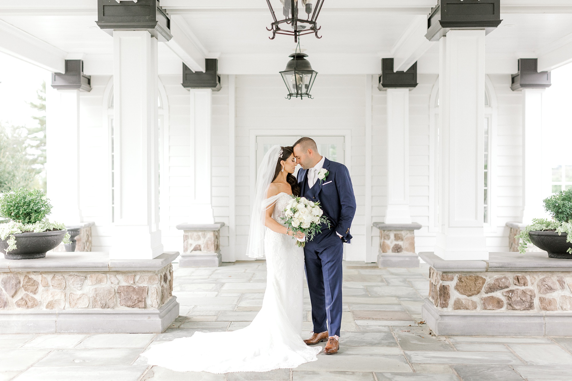 bride and groom hug under awning at Ryland Inn while bride holds white rose bouquet
