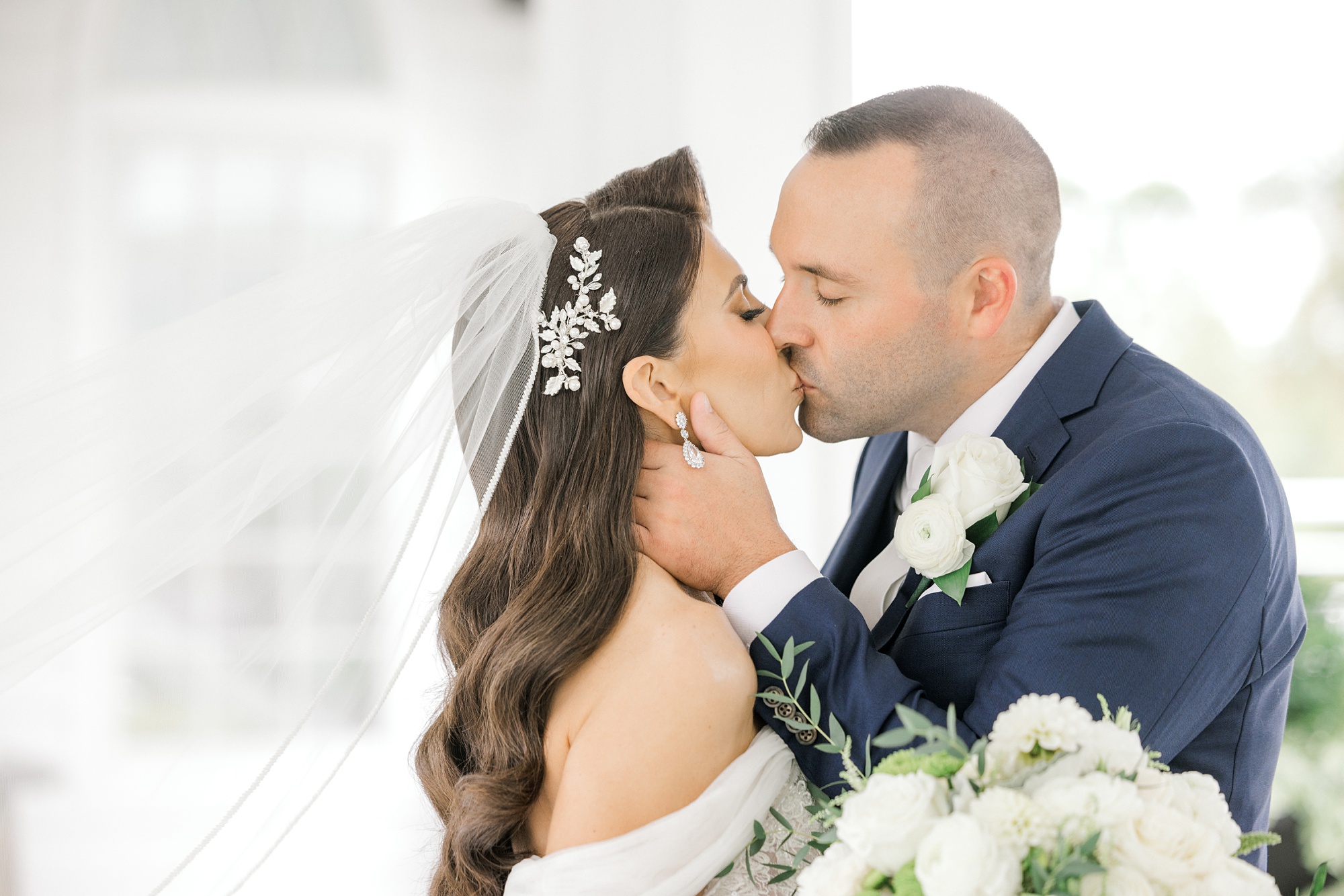 groom in navy suit leans to kiss bride with veil floating behind them