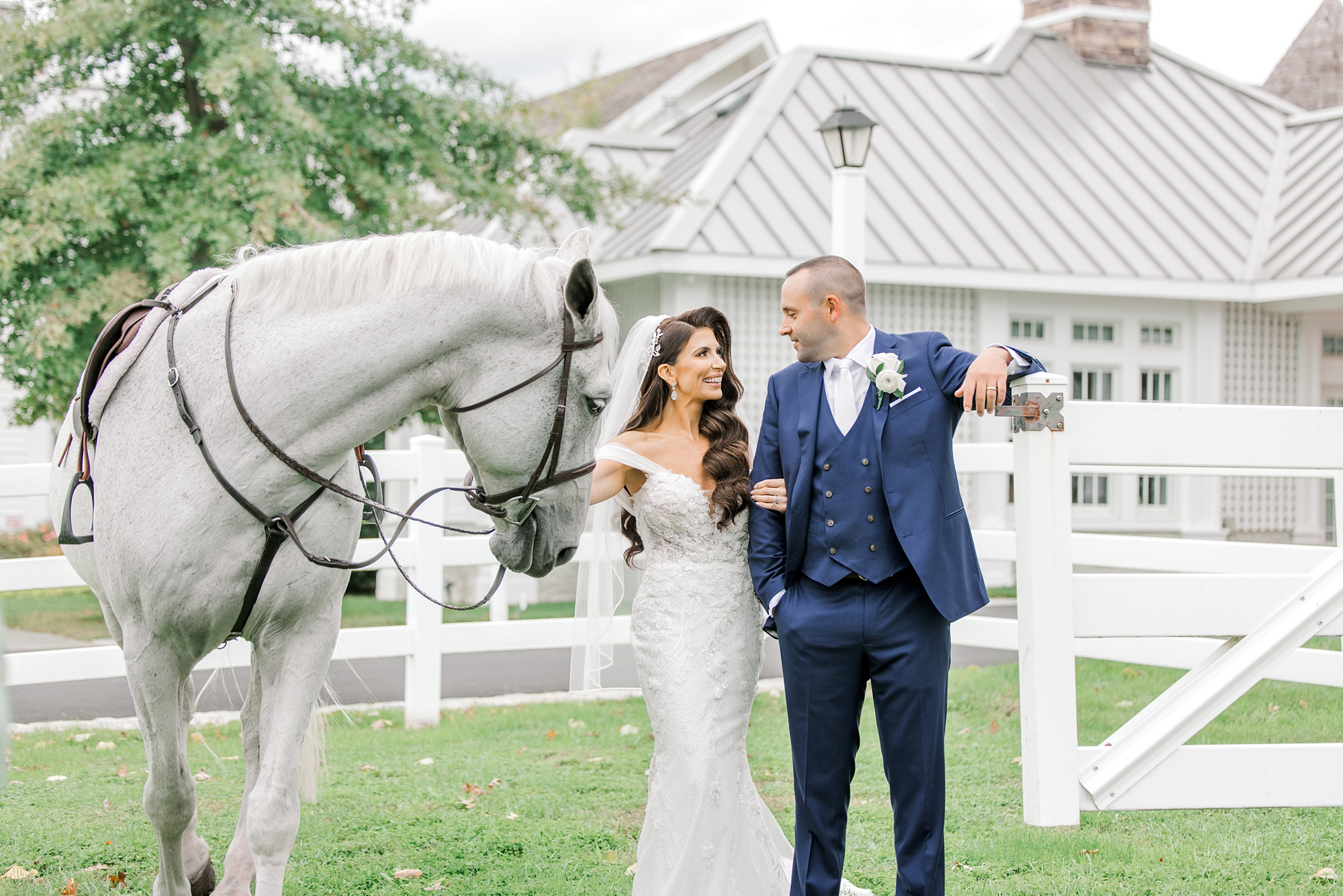 bride and groom hug while holding the reins of a white horse