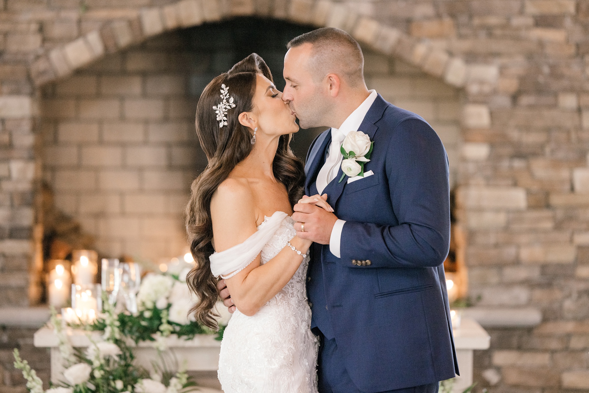 newlyweds kiss in front of stone fireplace with white candles inside
