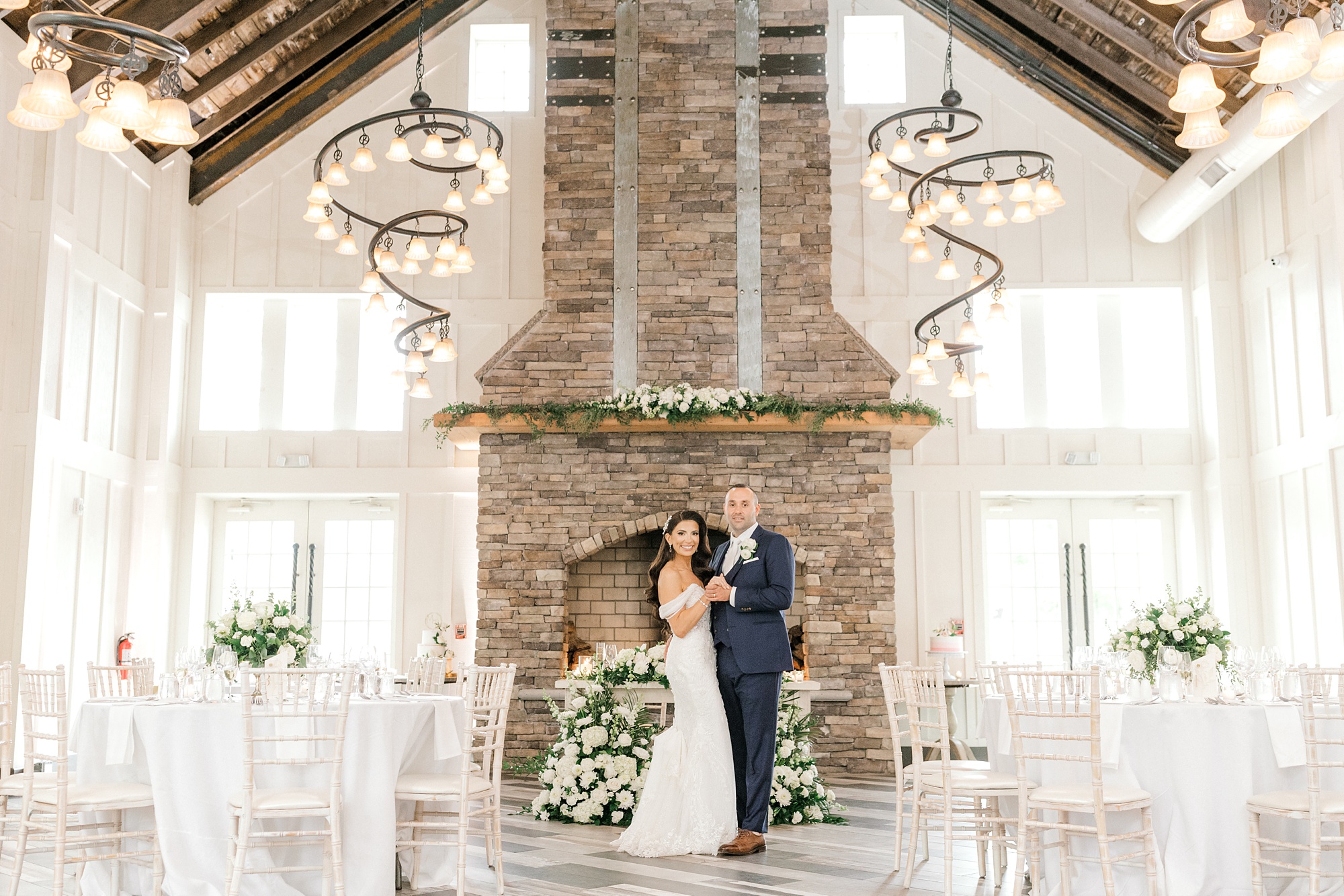 bride and groom pose in front of stone fireplace among reception setup at Ryland Inn