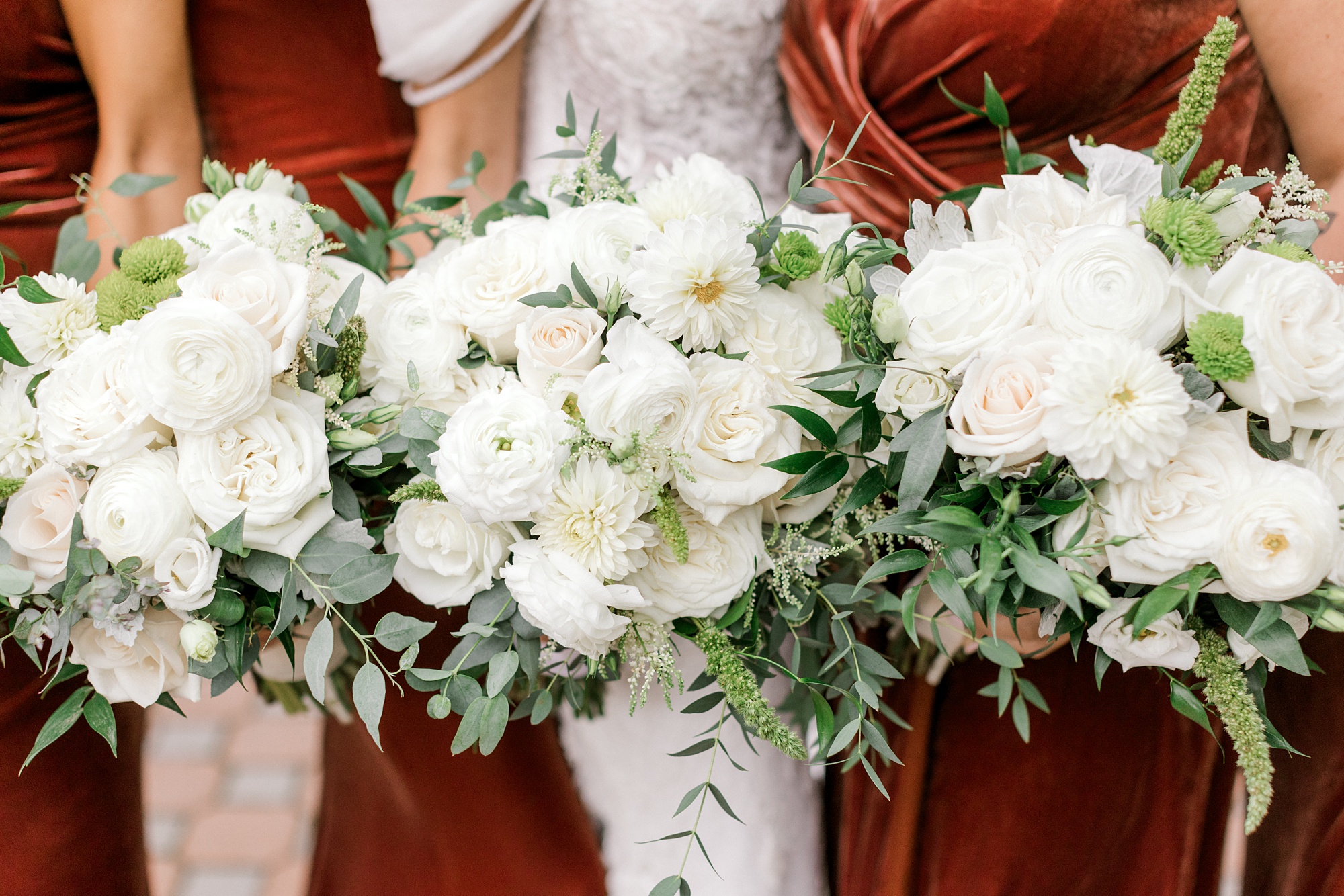 bride holds bouquet of white roses with red bridesmaid dresses for fall wedding at Ryland Inn