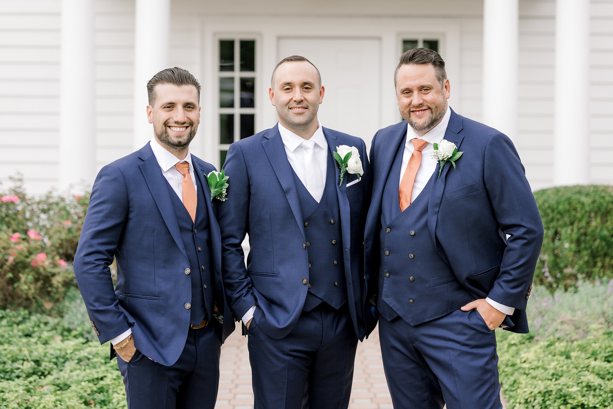 groom poses with two groomsmen in navy suits outside Ryland Inn