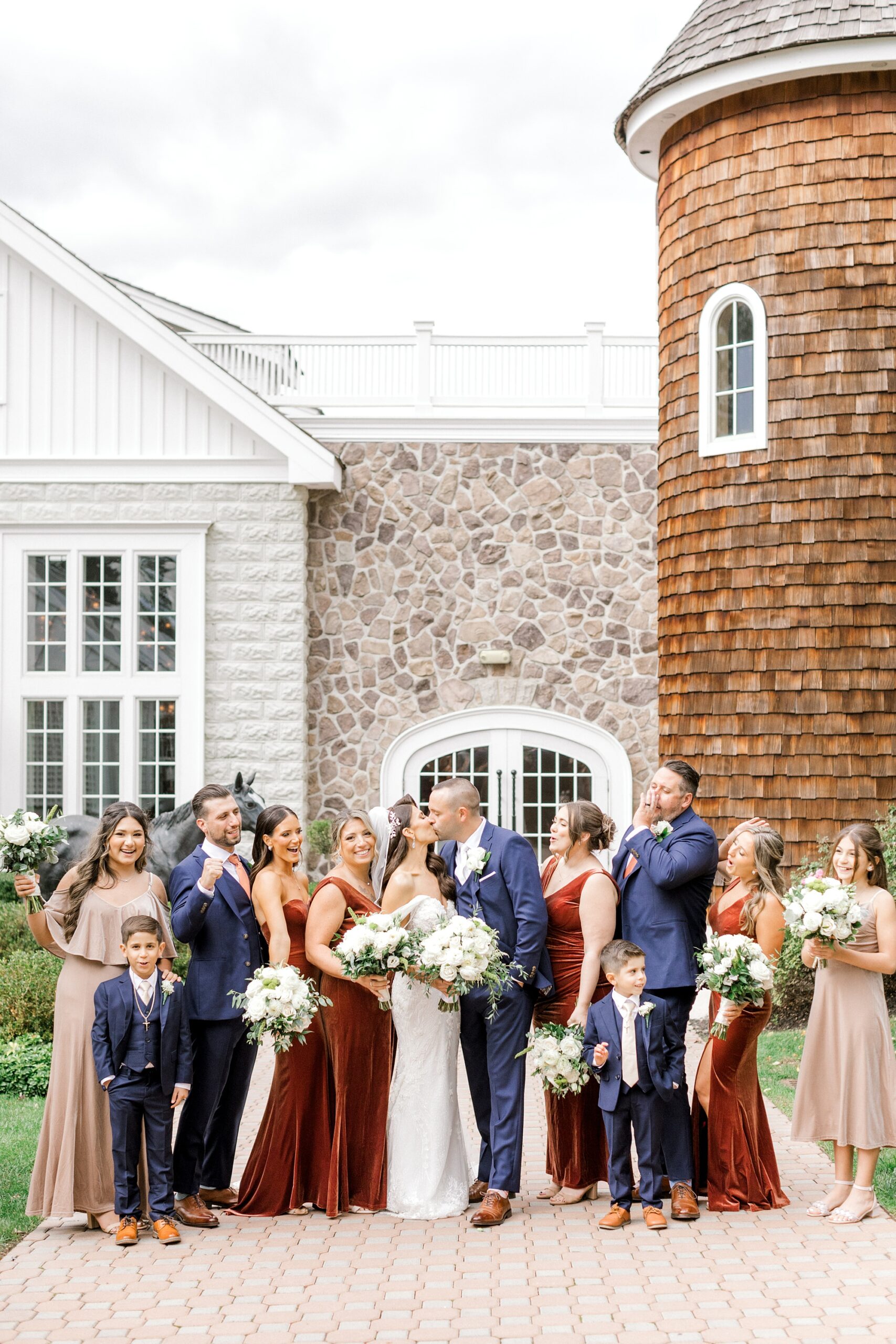 newlyweds hug with wedding party in navy suits and red velvet gowns outside Ryland Inn