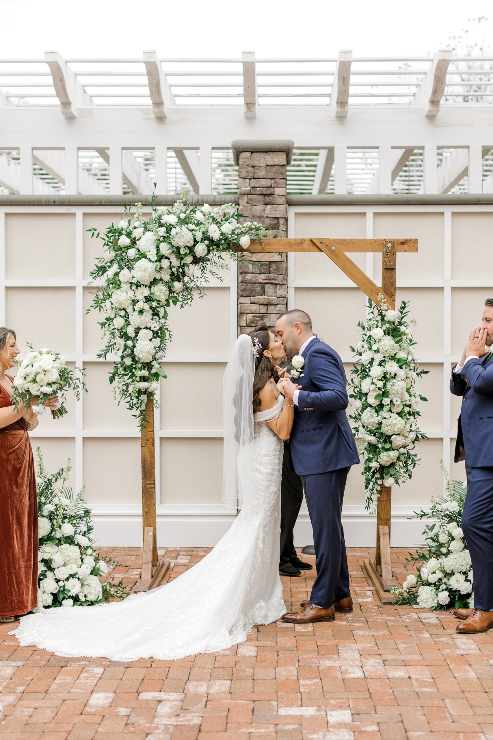newlyweds kiss under wooden arbor with white flowers during wedding ceremony at Ryland Inn on the patio