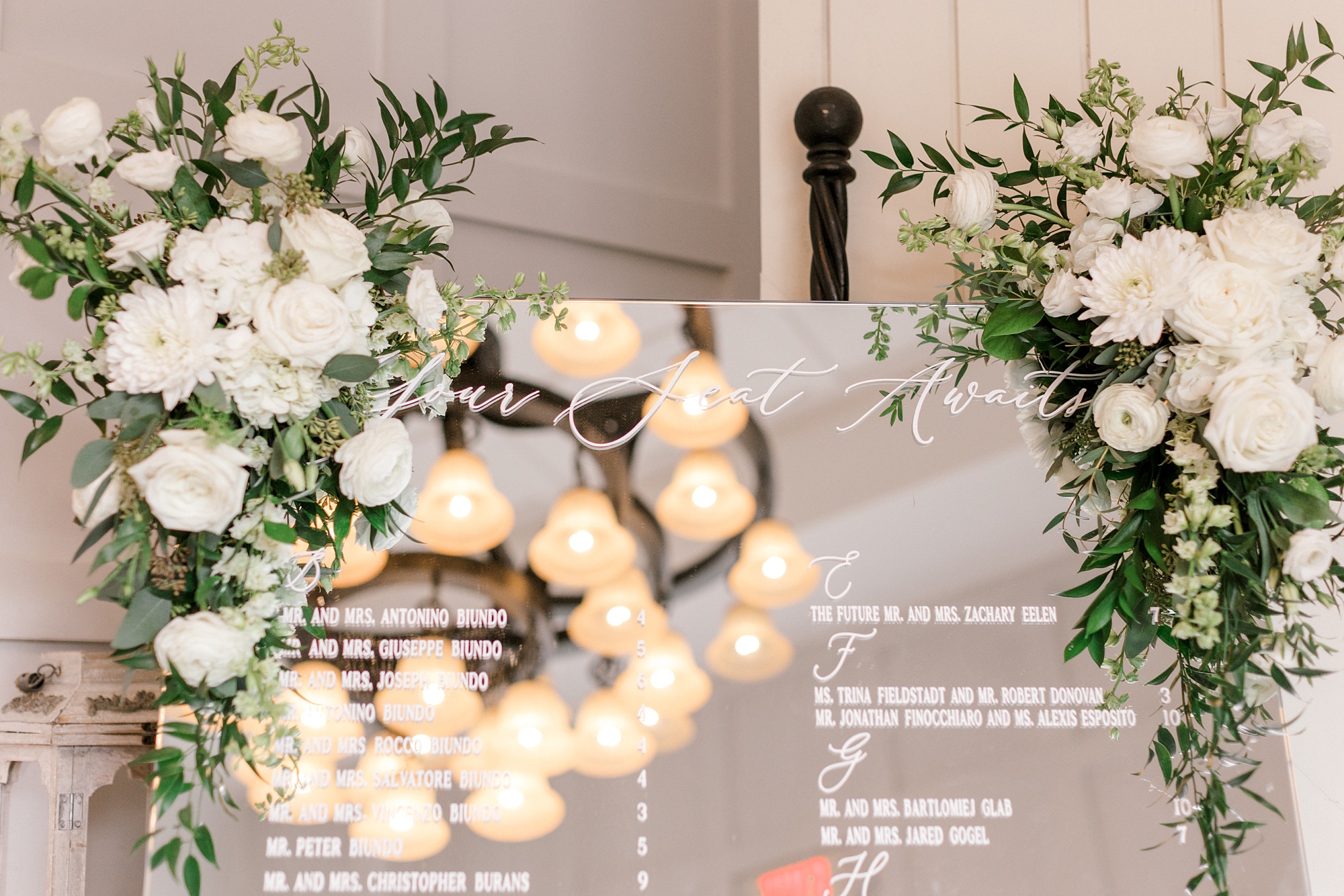 seating chart on mirror with white flowers along top