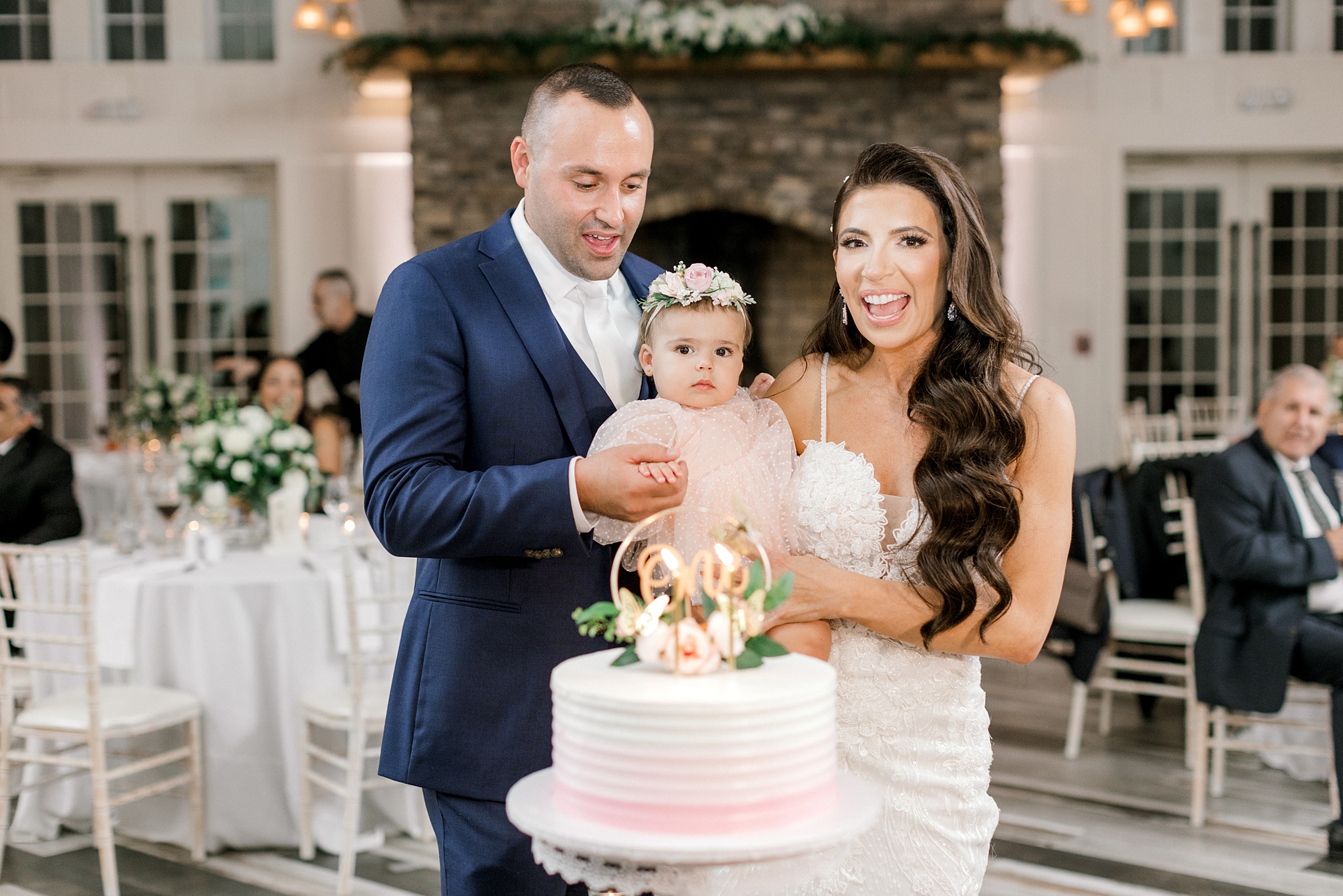 bride and groom pose with one year old daughter to cut wedding cake at wedding reception at Ryland Inn