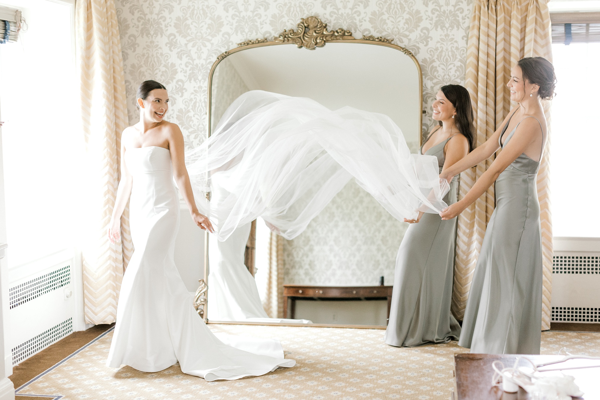 bridesmaids fluff out veil for bride in front of mirror inside suite at Fiddler's Elbow Country Club