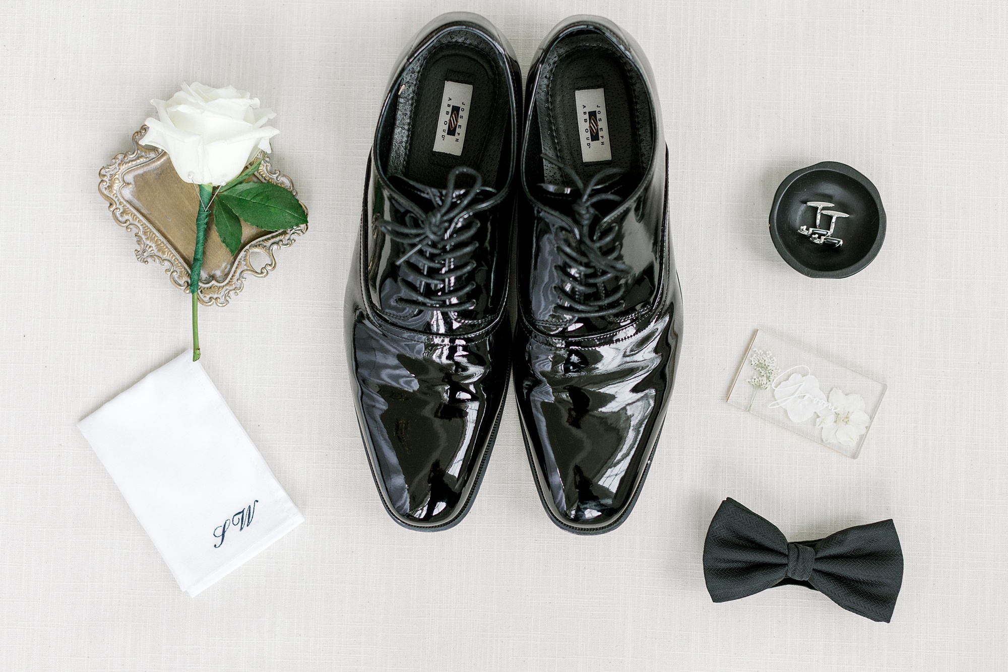 groom's black shoes, white boutonnière, and black bow tie