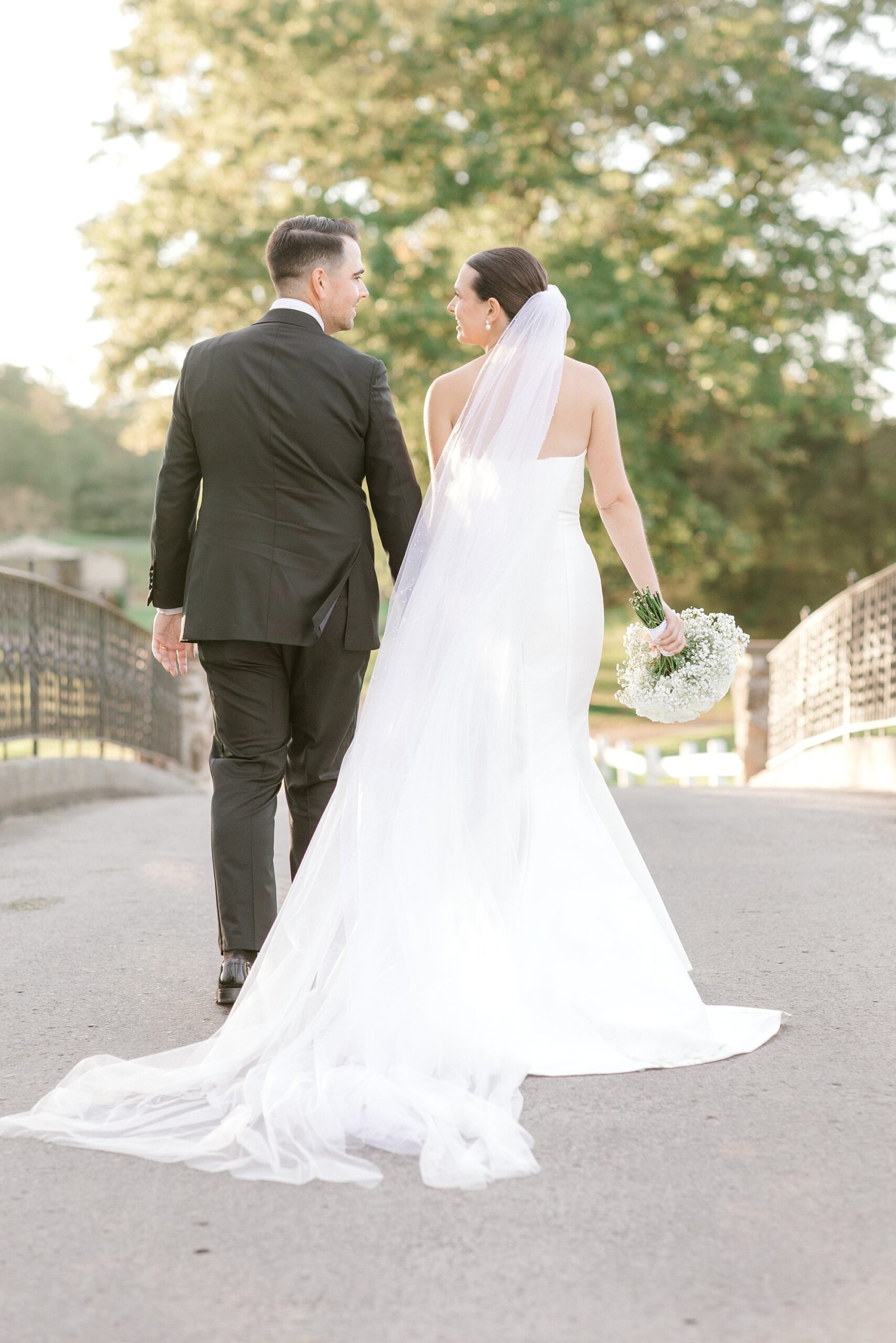 bride and groom hold hands walking over bridge at Fiddler’s Elbow Country Club 