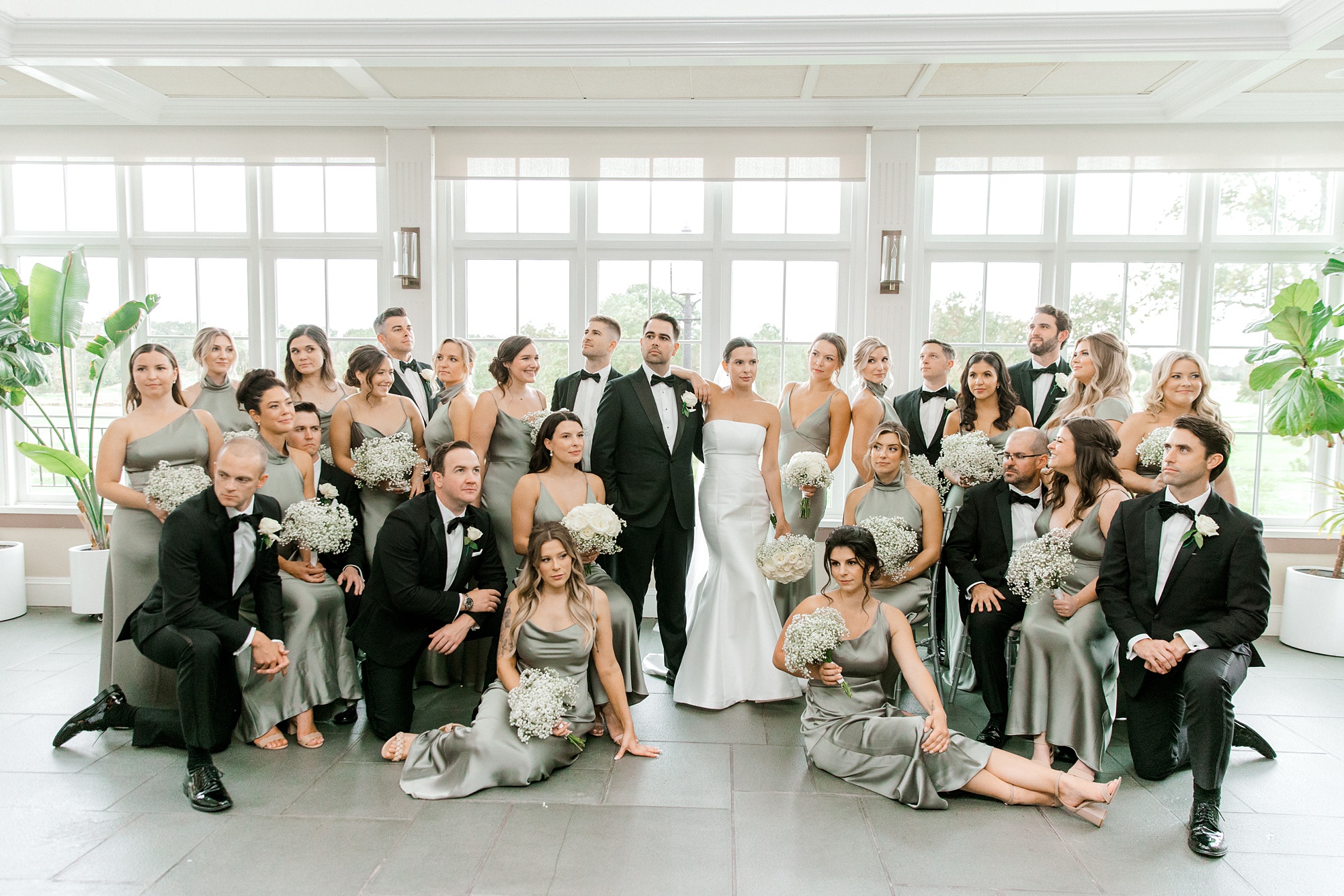 newlyweds pose with large wedding party inside conservatory at Fiddler’s Elbow Country Club 