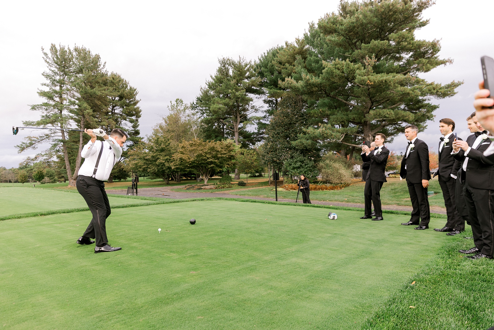 groomsmen watch groom swing golf club at Fiddler’s Elbow Country Club 