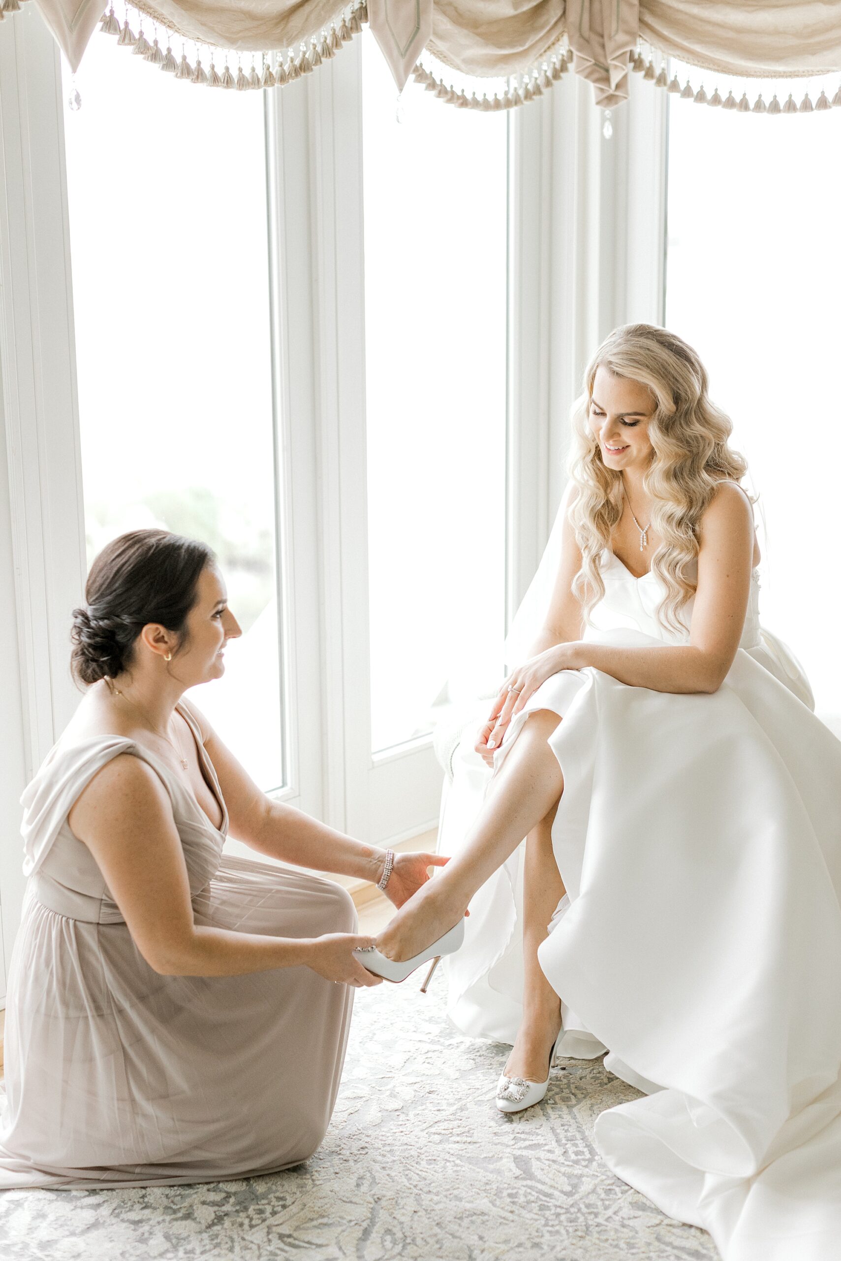 bridesmaid helps bride with shoes inside suite at Bonnet Island Estate
